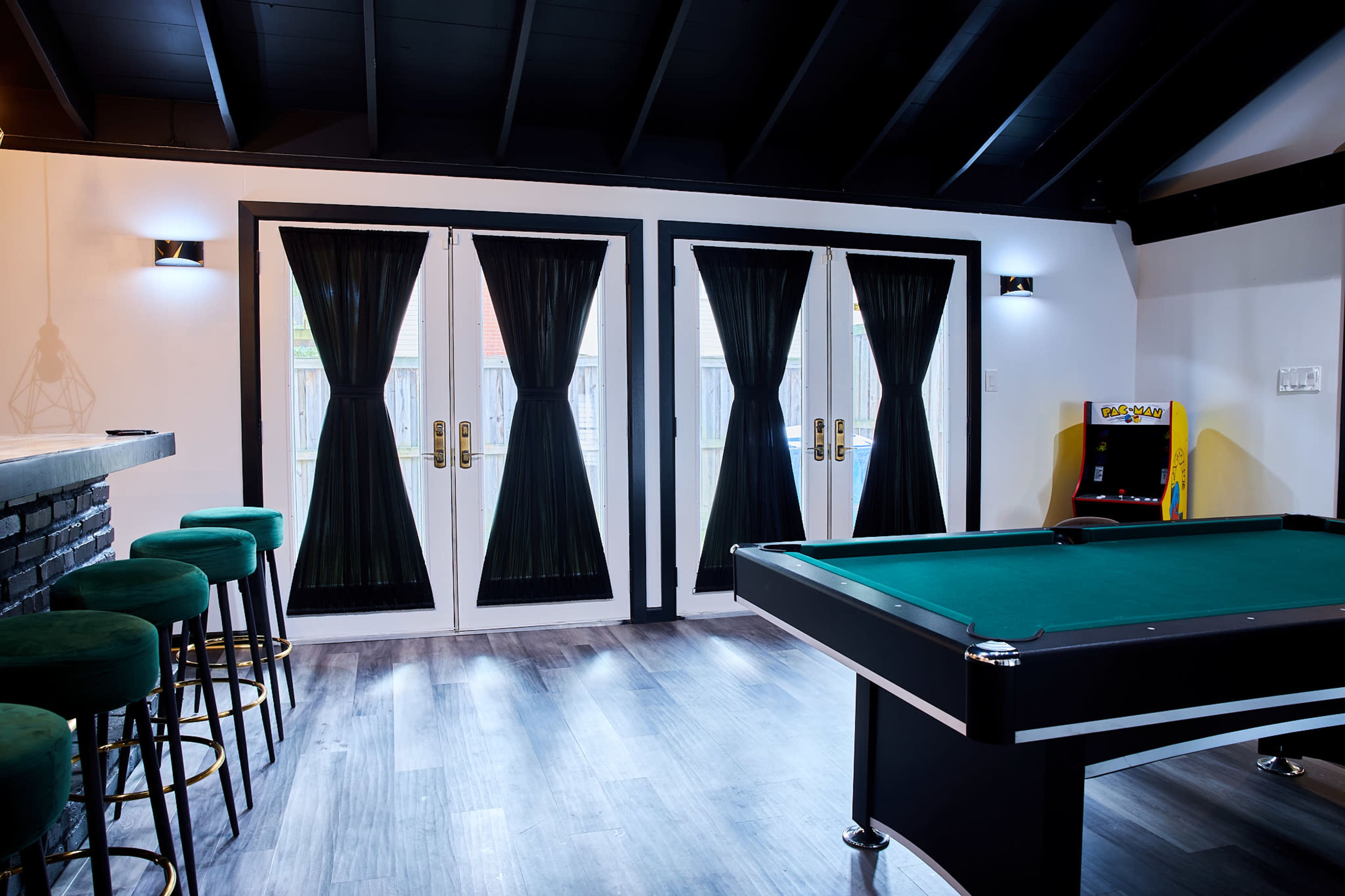 A game room features a pool table, bar stools, and double French doors with black curtains.