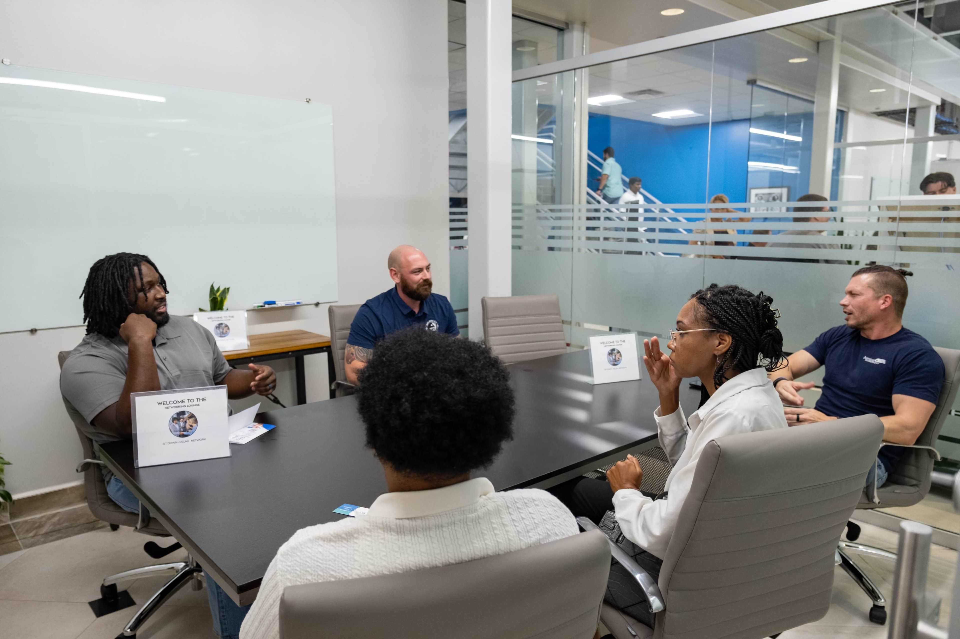 A group of five individuals are seated around a conference table in a modern office setting, engaged in discussion.