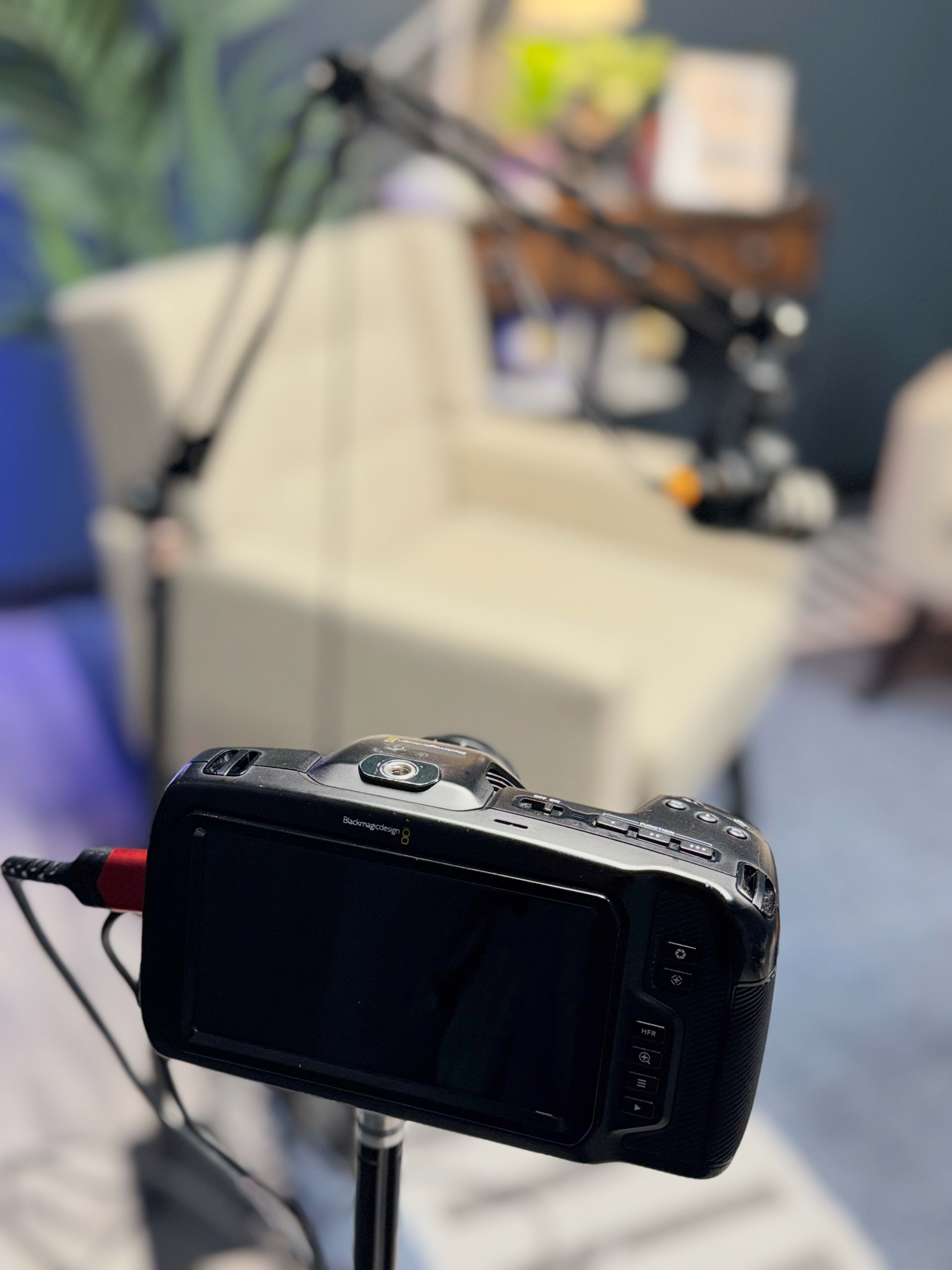 A camera is positioned on a tripod facing a light-colored chair in a studio setting.