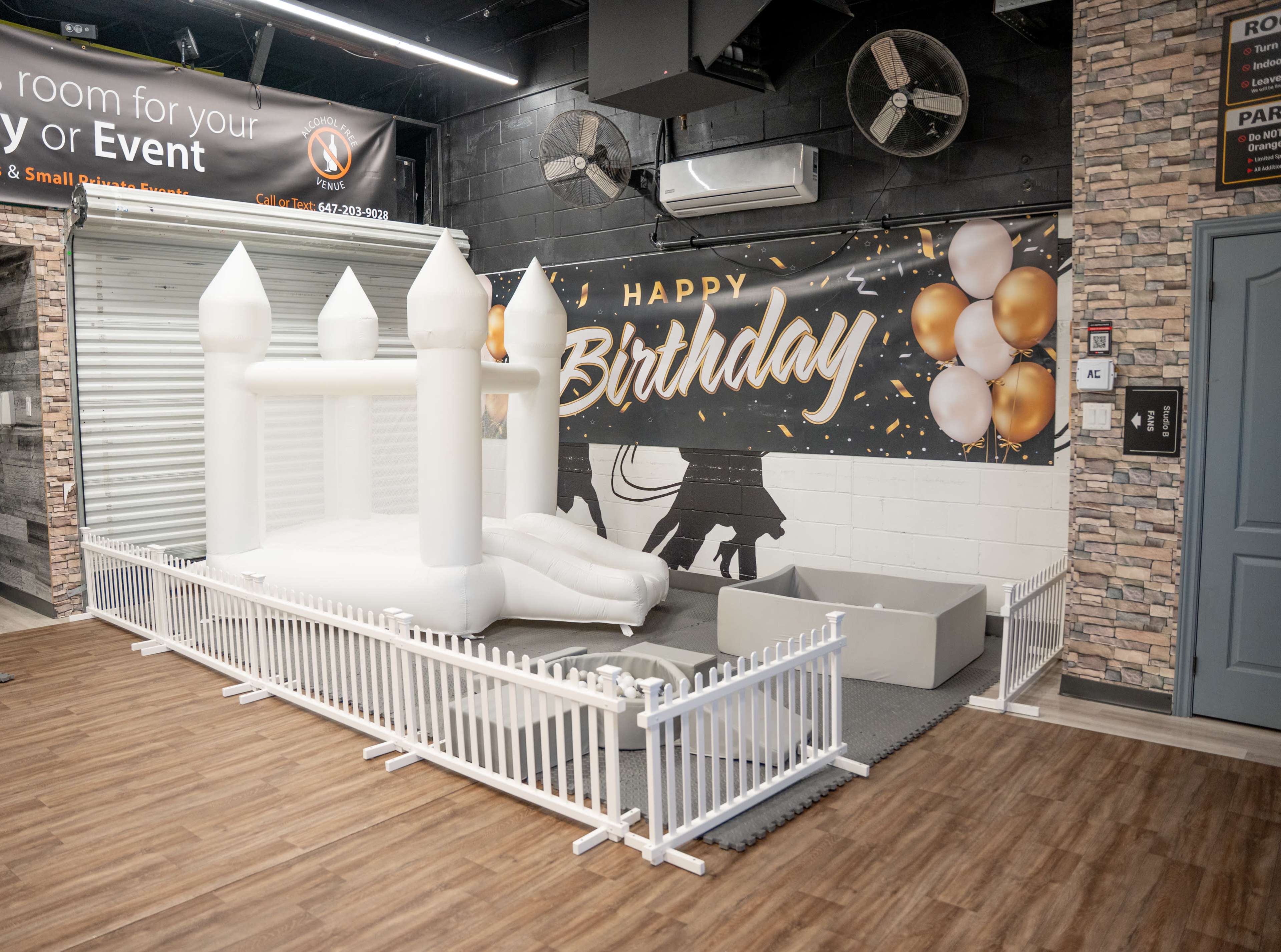 A white inflatable bounce house with a slide is set up in a decorated space featuring a "Happy Birthday" banner and balloons.