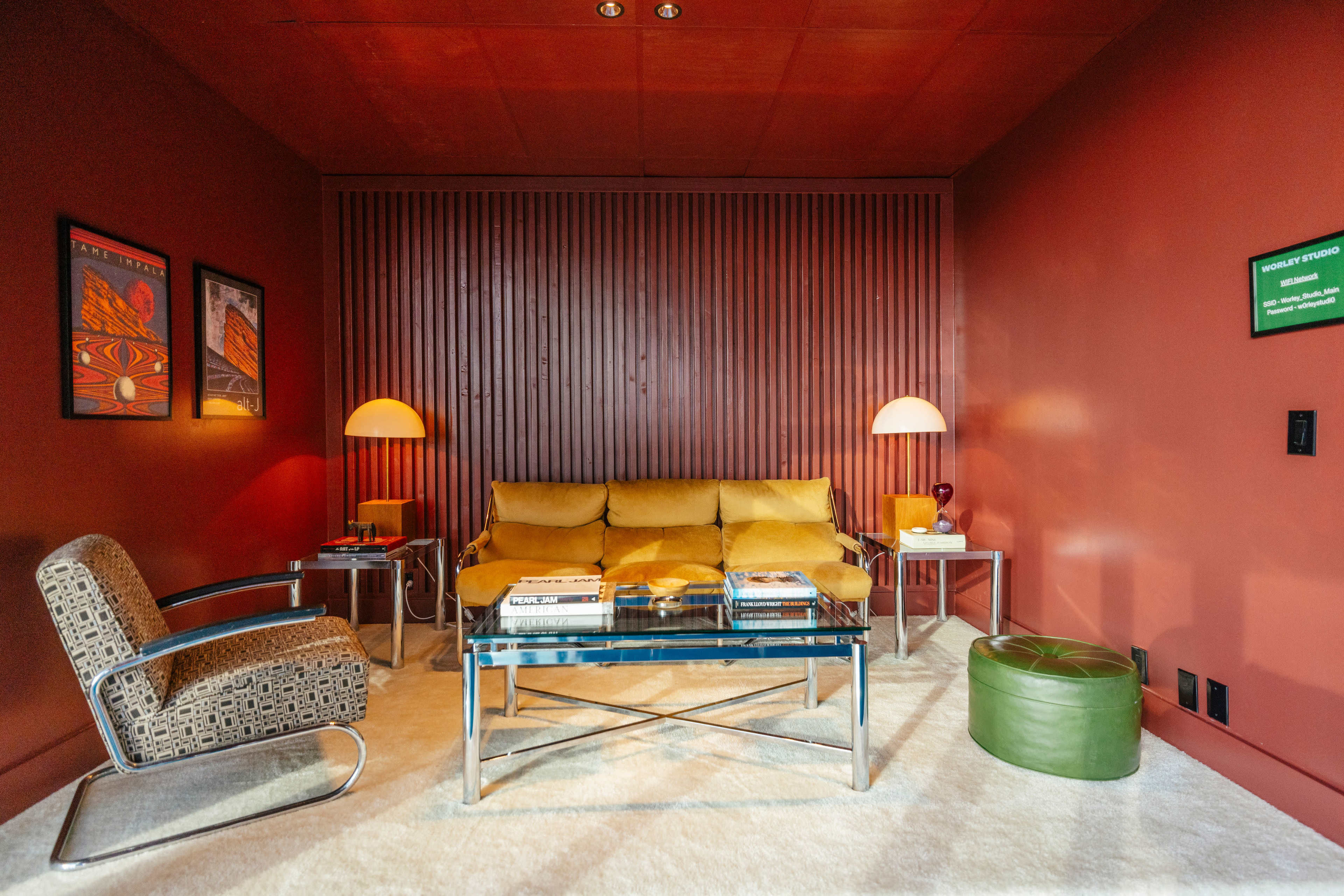 The image shows a modern living room with a yellow couch, a glass coffee table, and two stylish lamps, surrounded by red walls and decorative artwork.