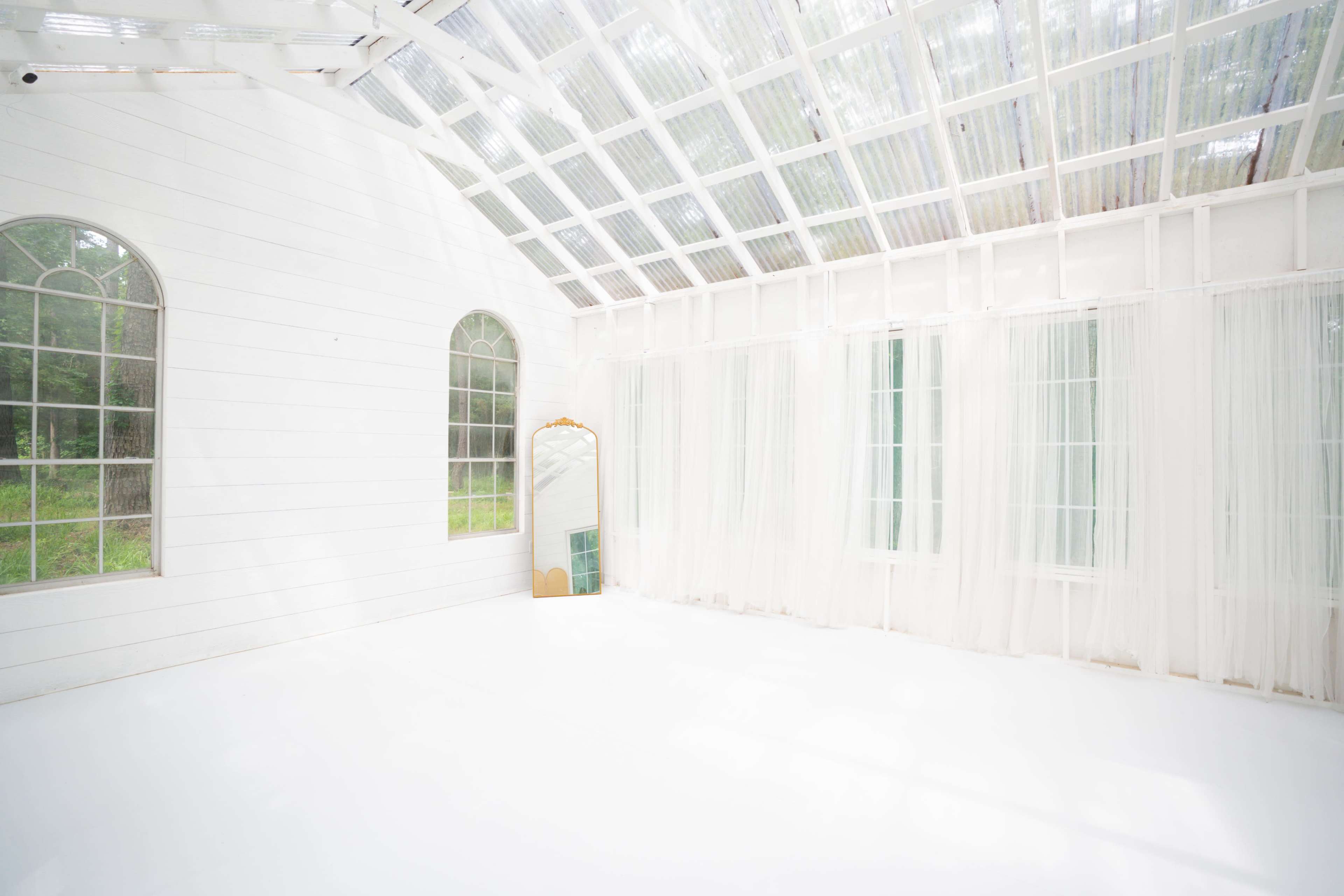 The image shows a bright, airy room with white walls, large windows, and sheer curtains, accompanied by a mirror and a minimalist aesthetic.