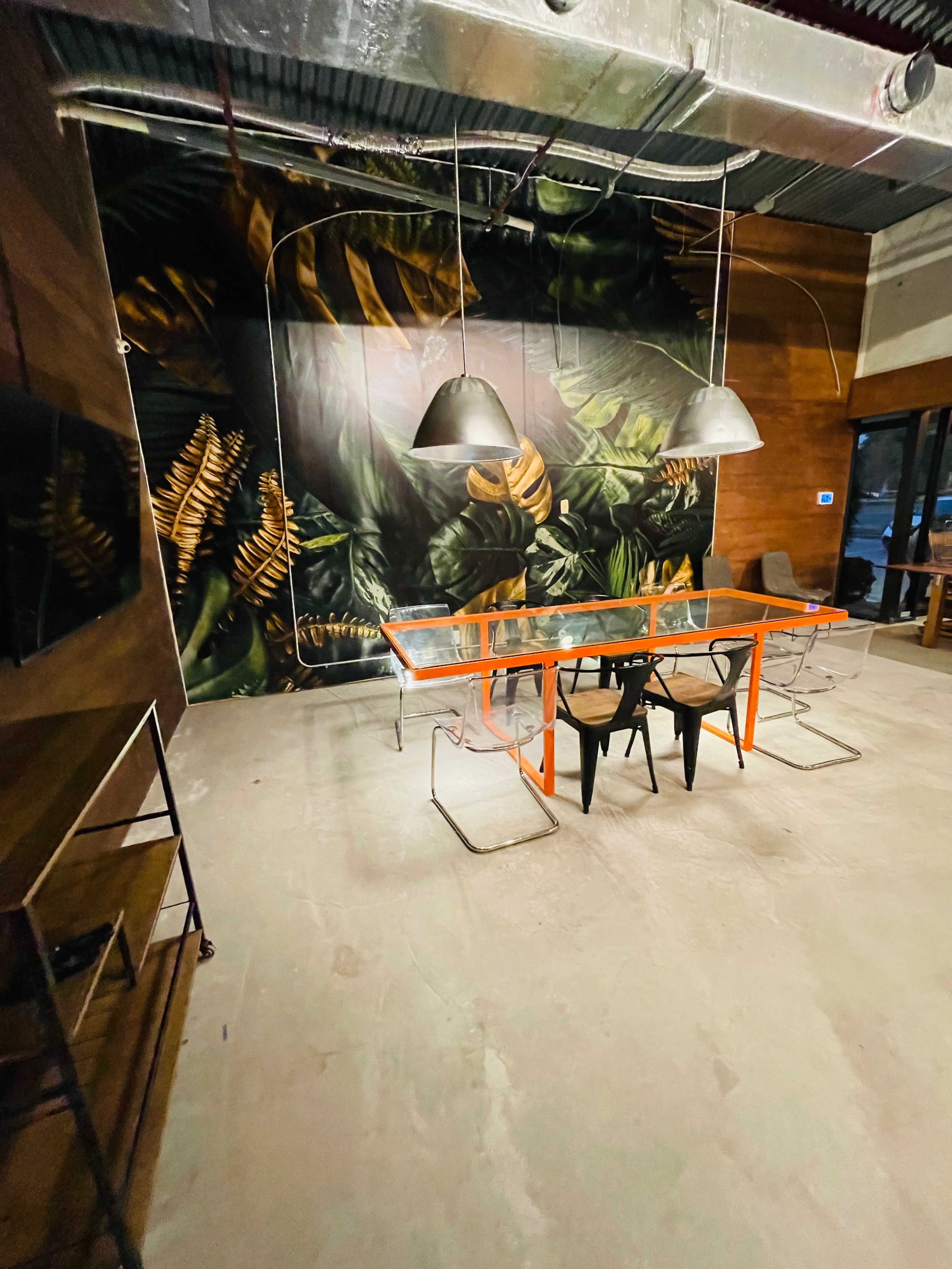 A modern conference room features a glass table surrounded by black chairs and pendant lights, with a large botanical mural on the wall.