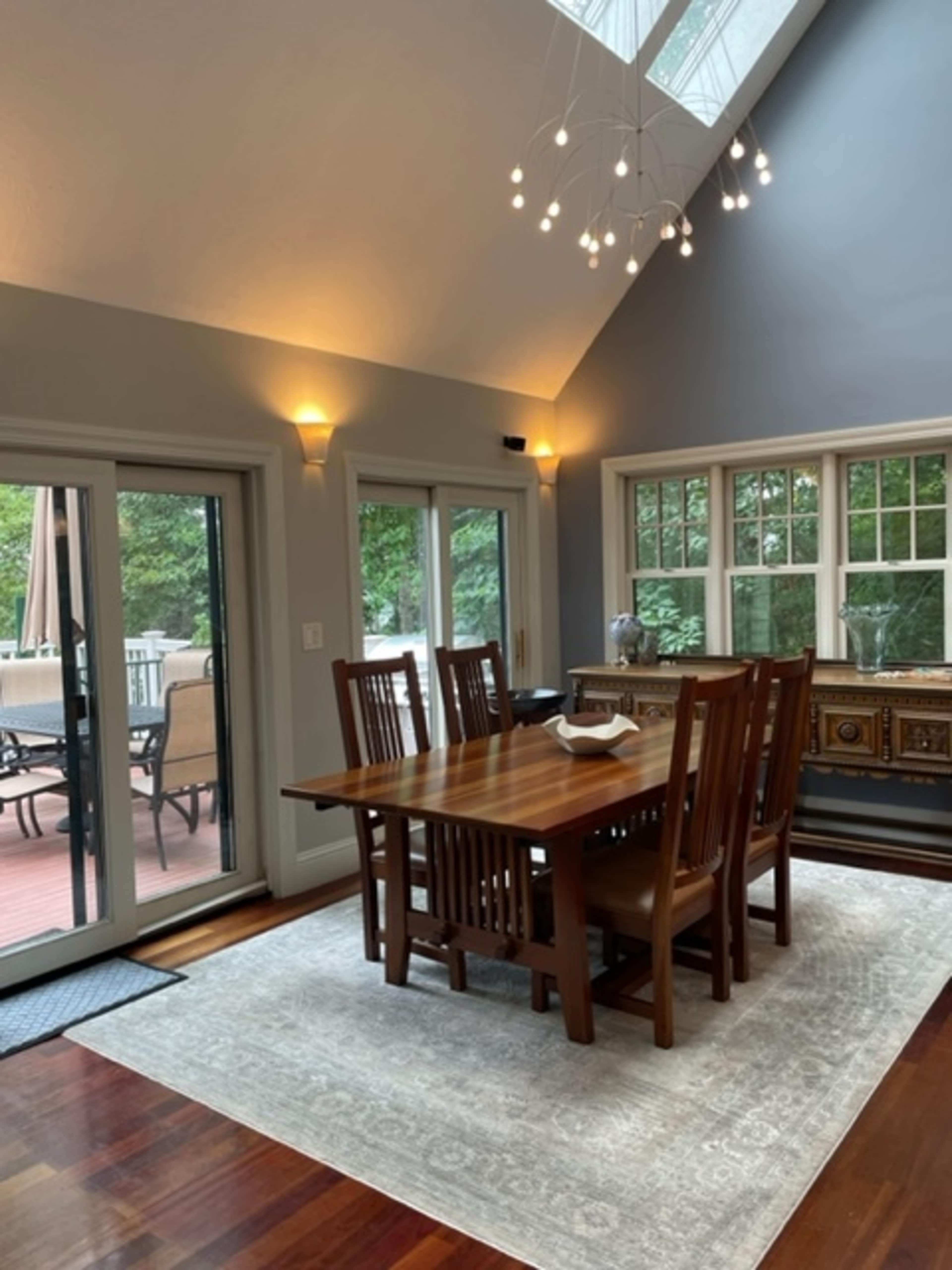 A dining area with a wooden table surrounded by chairs, situated under a skylight and illuminated by wall sconces.