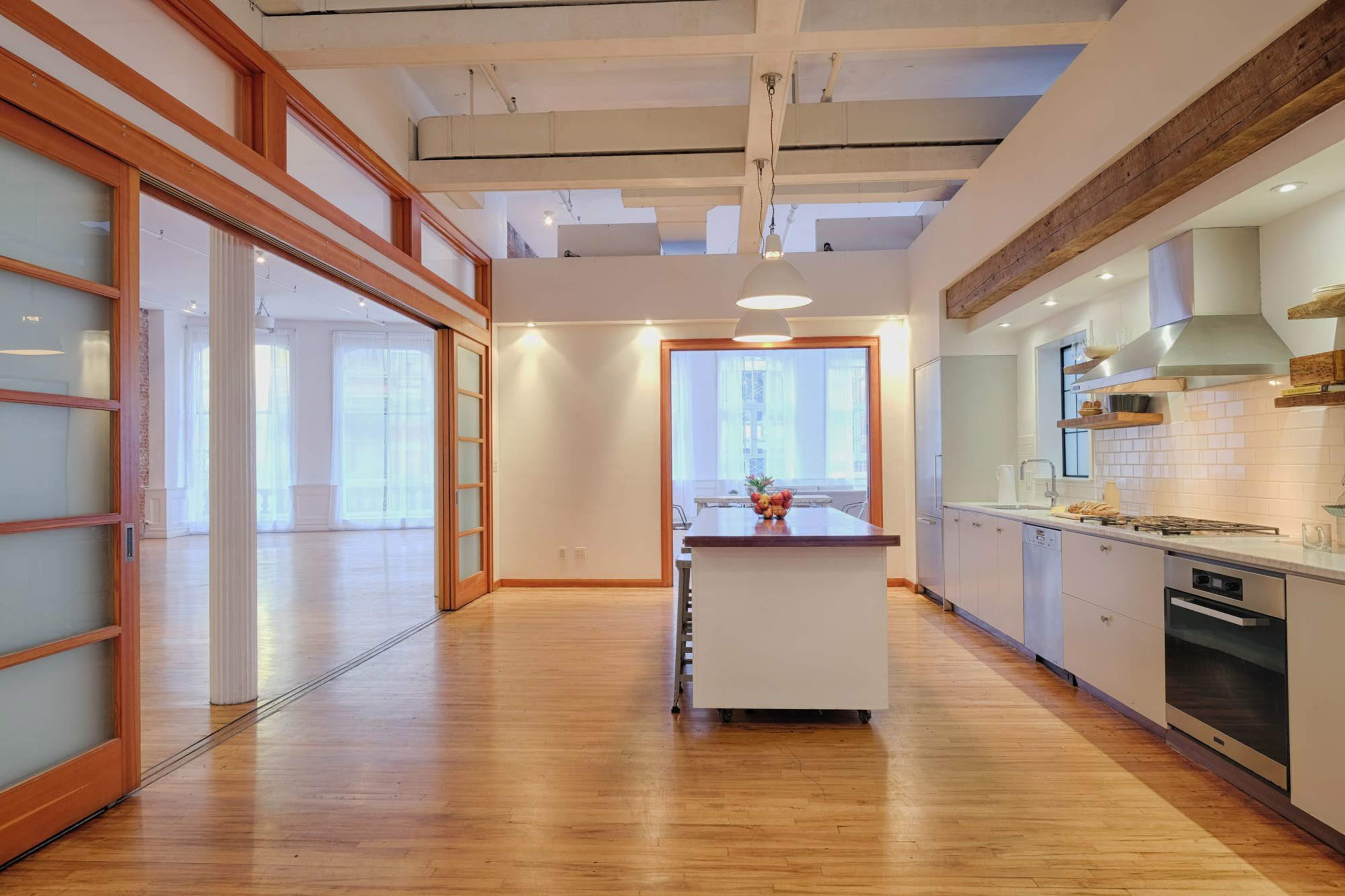 An open-concept kitchen area with wooden flooring, large windows, and a central island with seating.