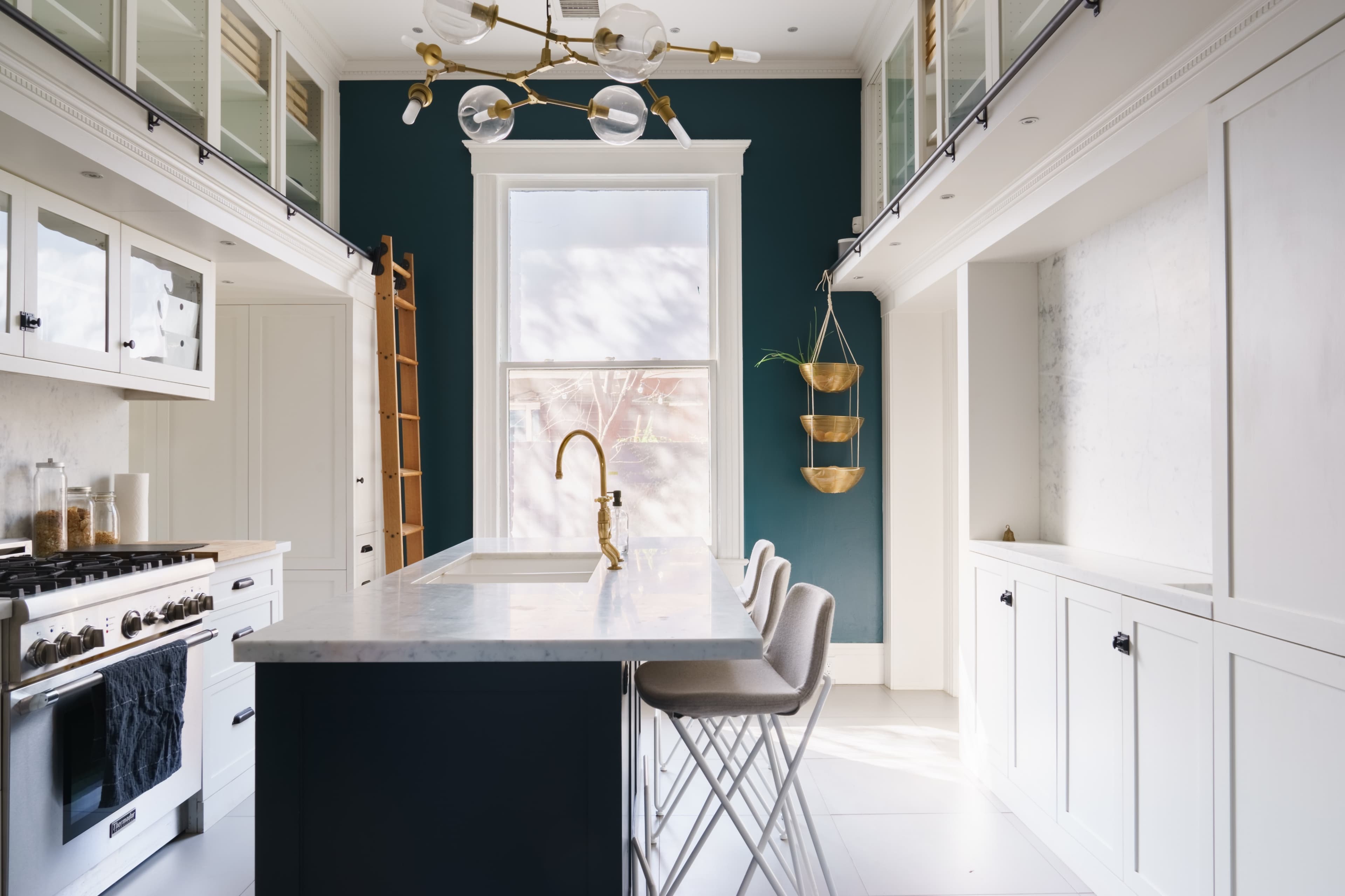 A modern kitchen with a dark green wall, marble countertops, and a three-seat bar area.