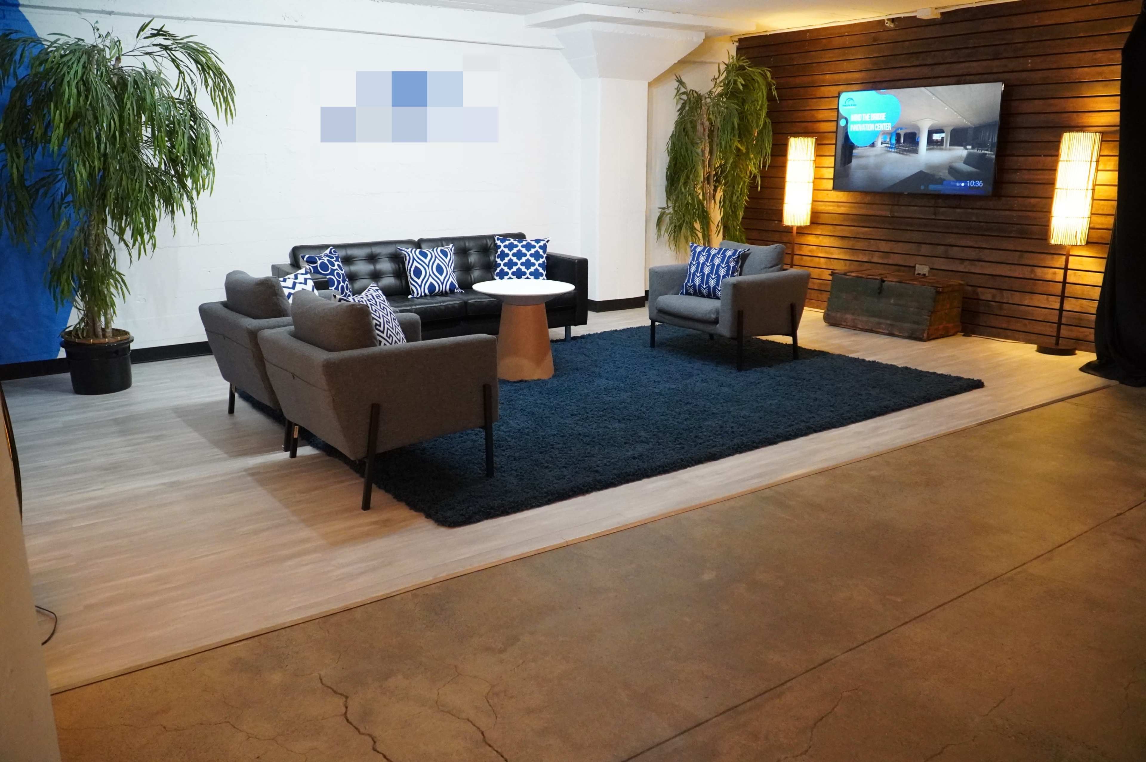 A modern lounge area featuring a dark rug, a circular table, two gray sofas, and a television mounted on a wooden wall.