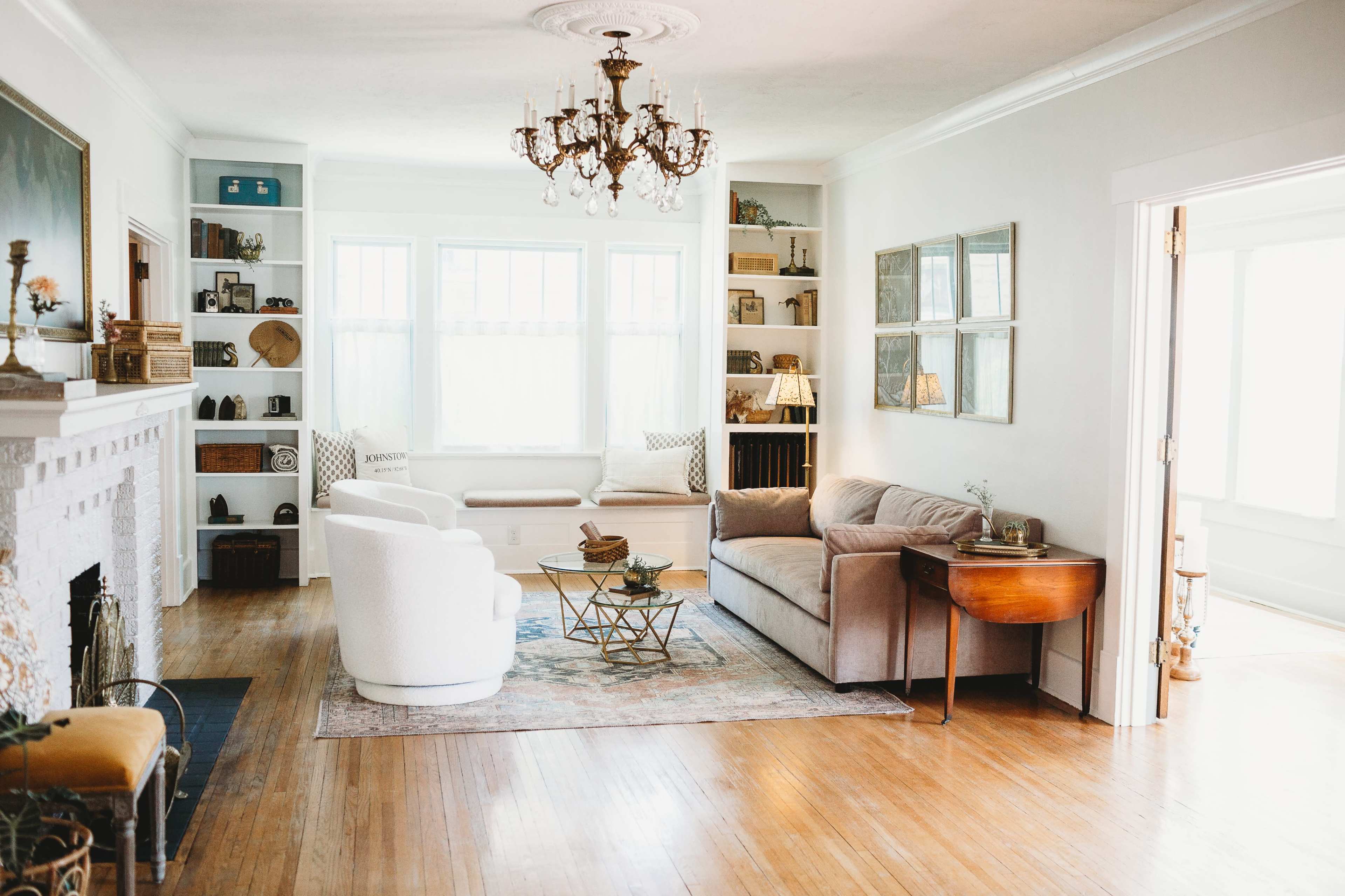 The living room features a chandelier, a white armchair, a beige sofa, a wooden coffee table, and built-in shelves filled with various decorative items.