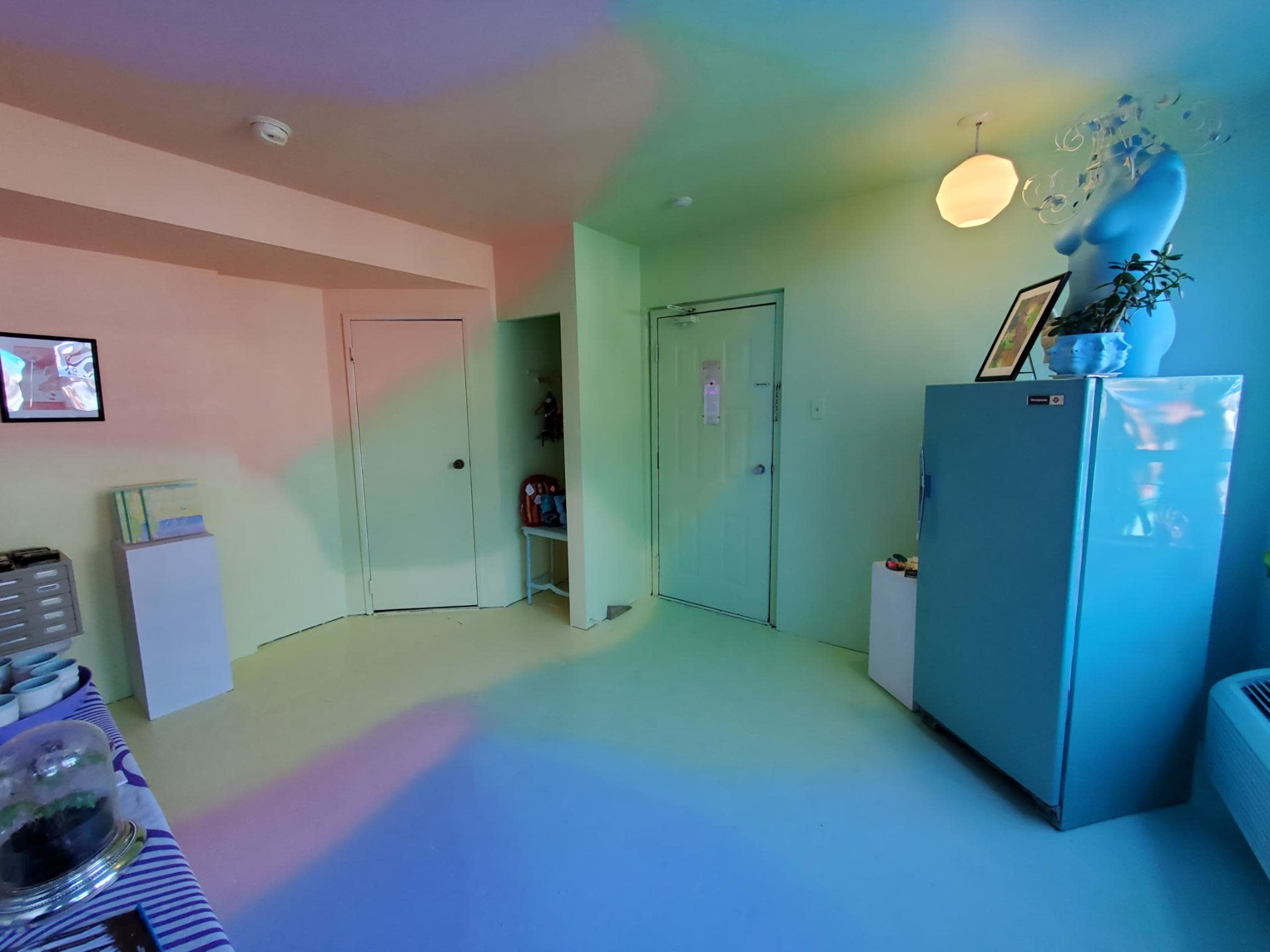 A brightly colored room with soft pastel walls, a blue refrigerator, and a small table against one wall.