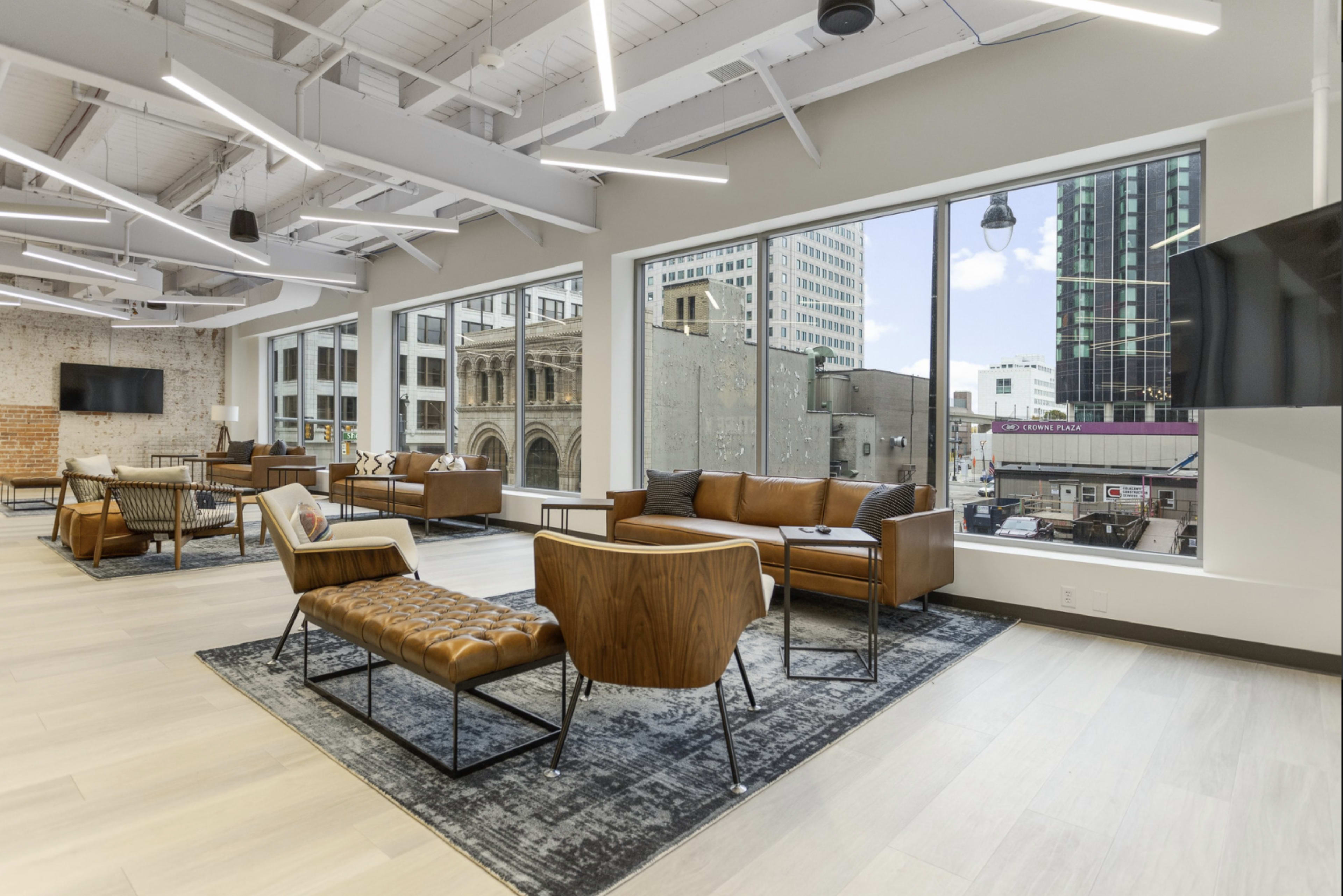 A modern lounge area with leather seating, large windows overlooking a cityscape, and minimalistic decor.