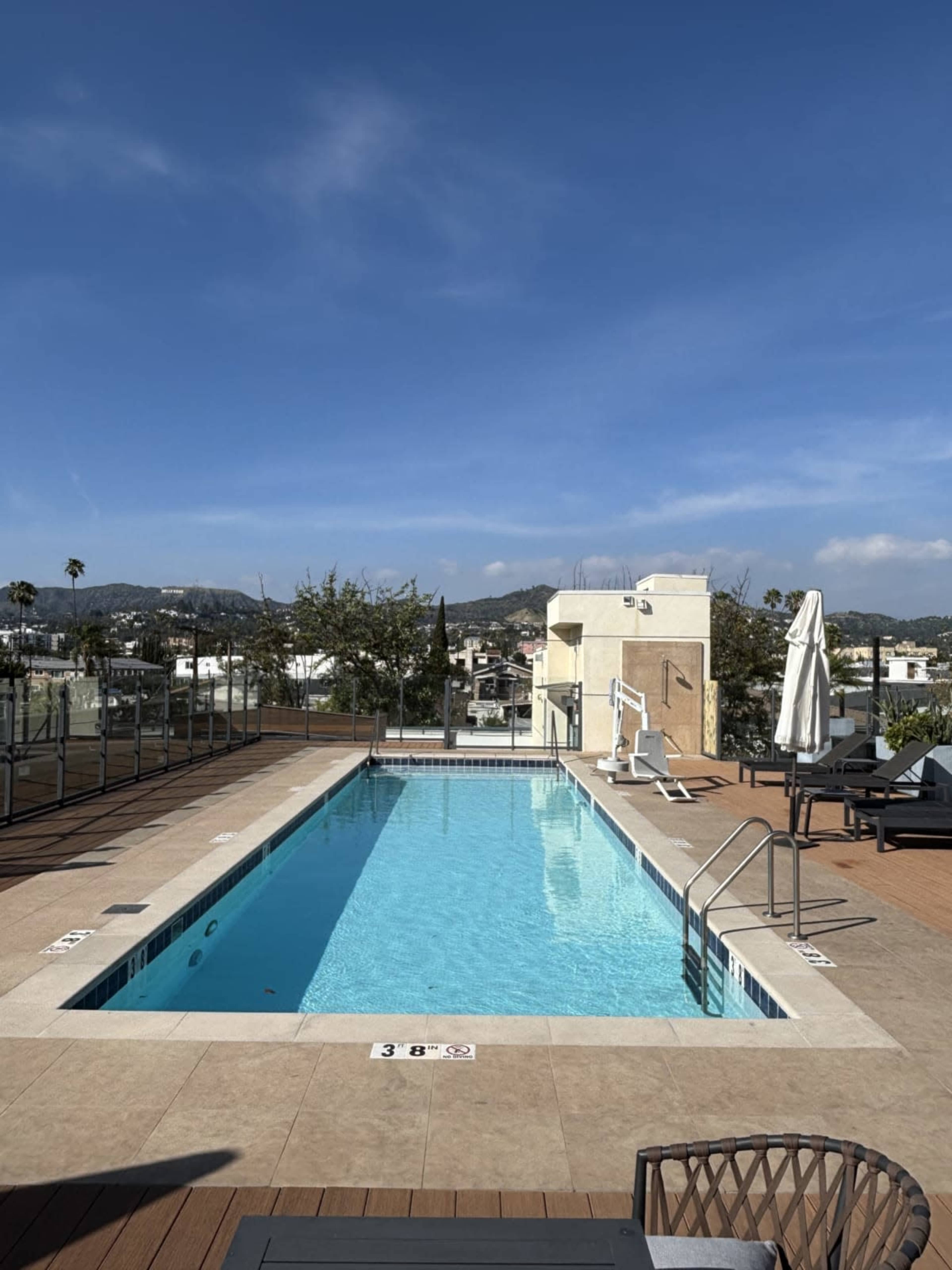 A rooftop swimming pool with a clear blue sky and surrounding cityscape in the background.