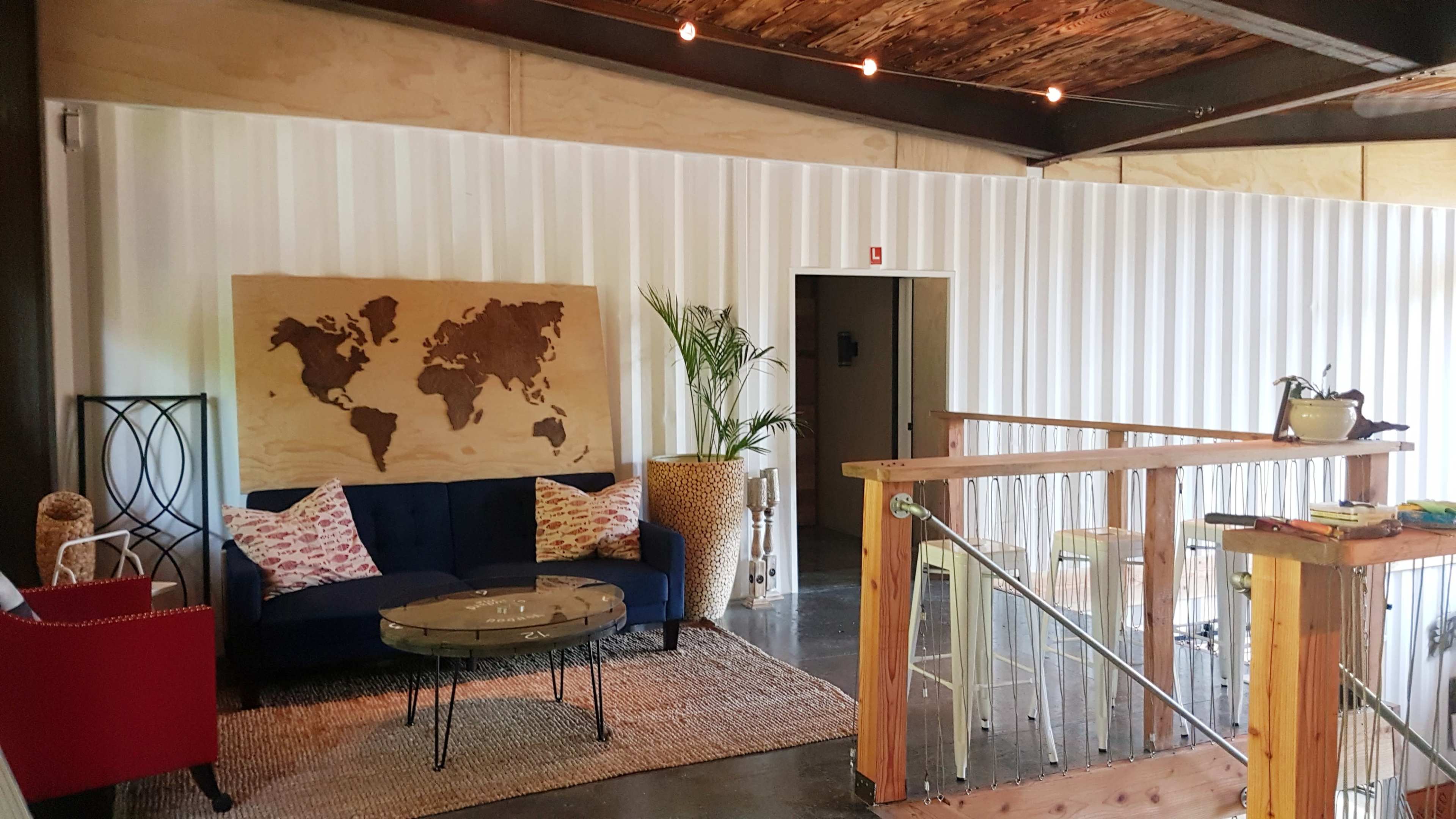 A cozy lounge area features a blue sofa, a world map on the wall, and a wooden railing overlooking a lower level.