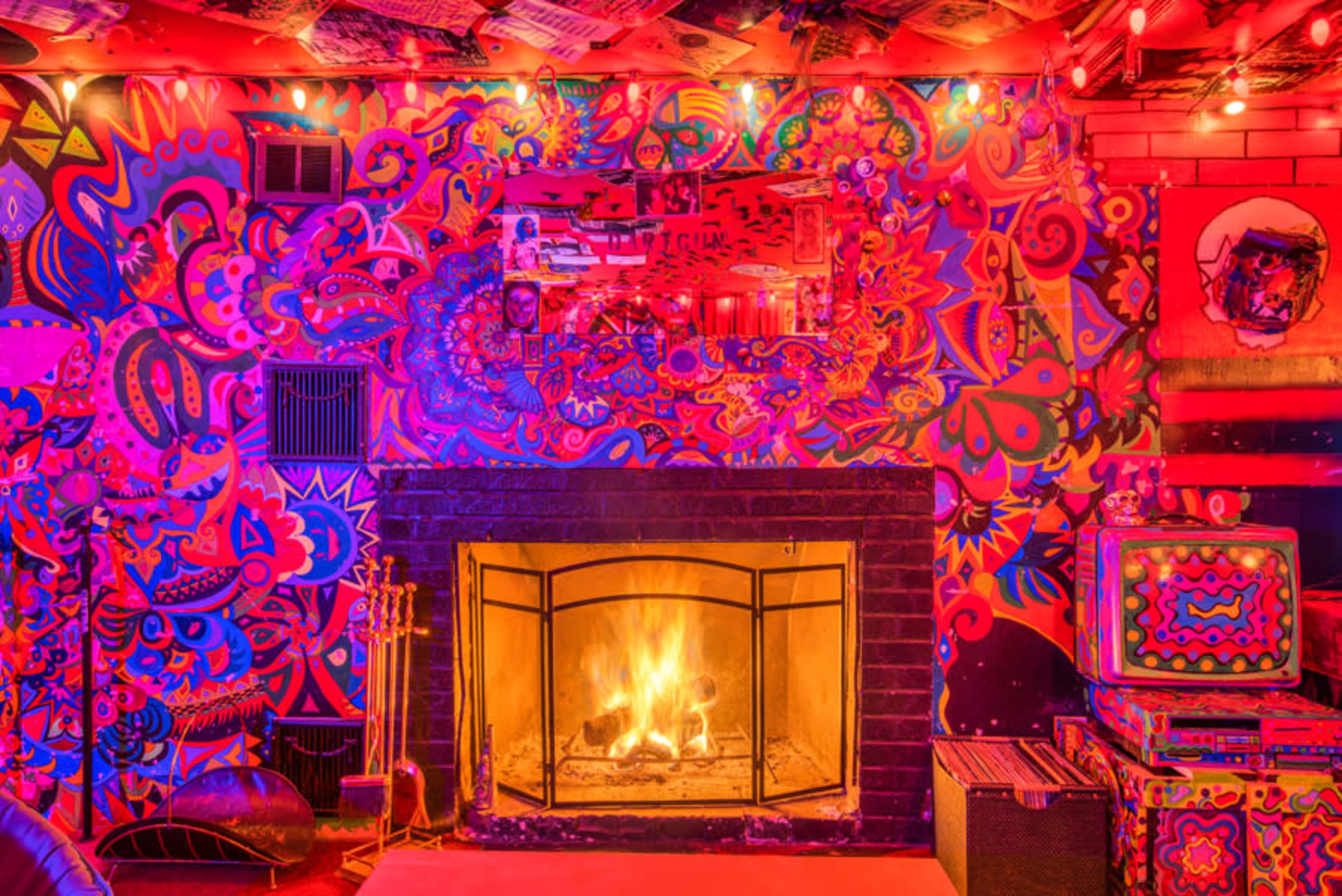A brightly colored room with a decorative fireplace surrounded by vibrant, psychedelic artwork on the walls.