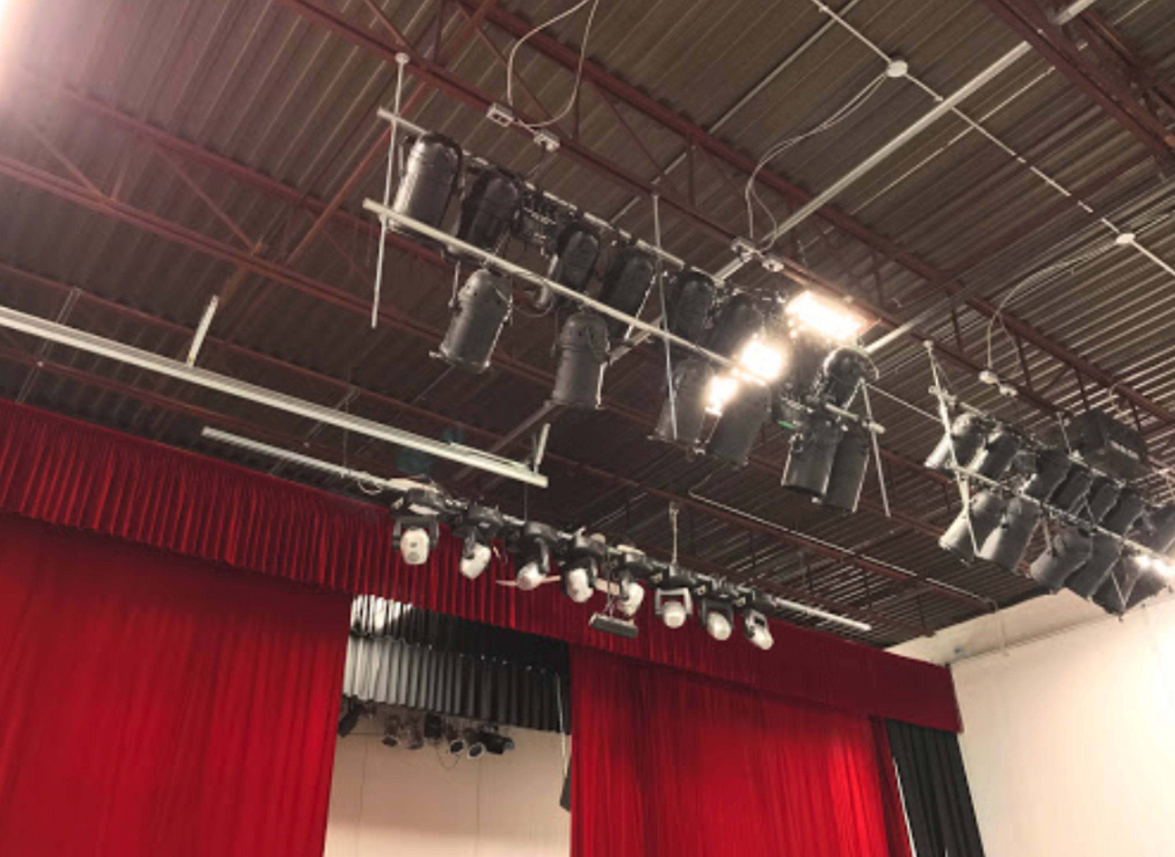 A stage setup with overhead lighting fixtures and red curtains in a performance space.
