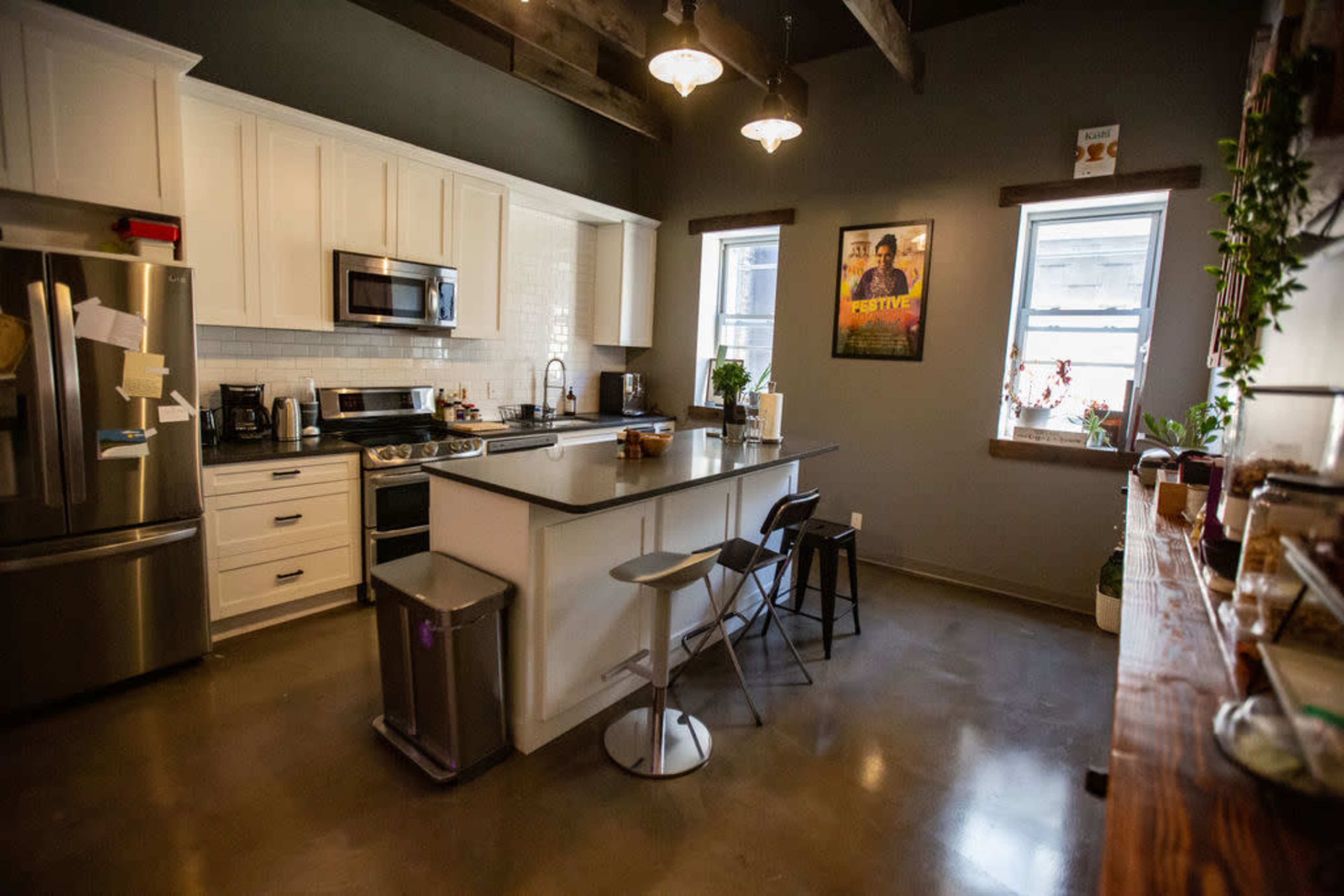 The image shows a modern kitchen with stainless steel appliances, white cabinetry, and a central island with two stools.