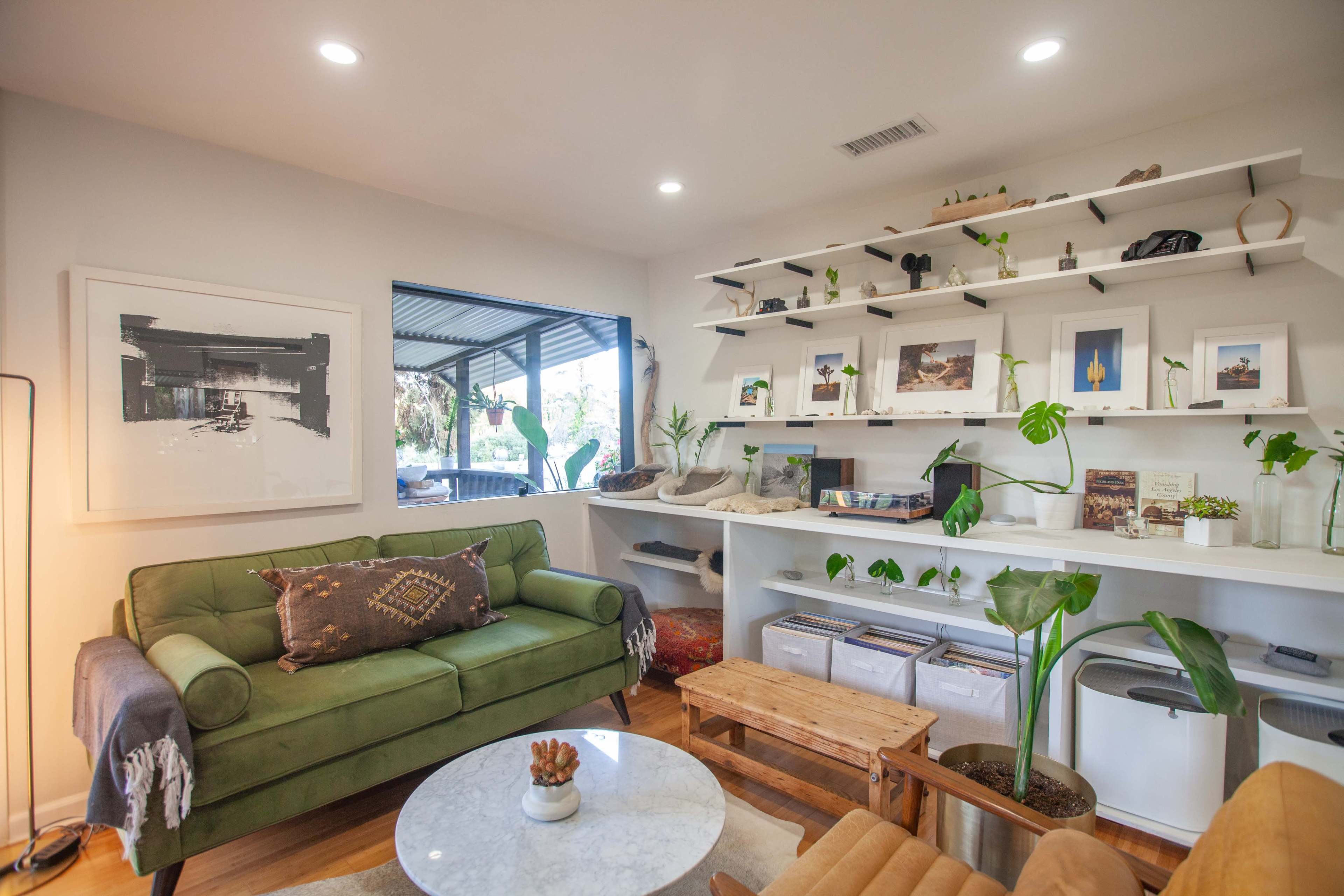 A cozy living area featuring a green sofa, a round marble coffee table, and shelves adorned with various decorative items and plants.