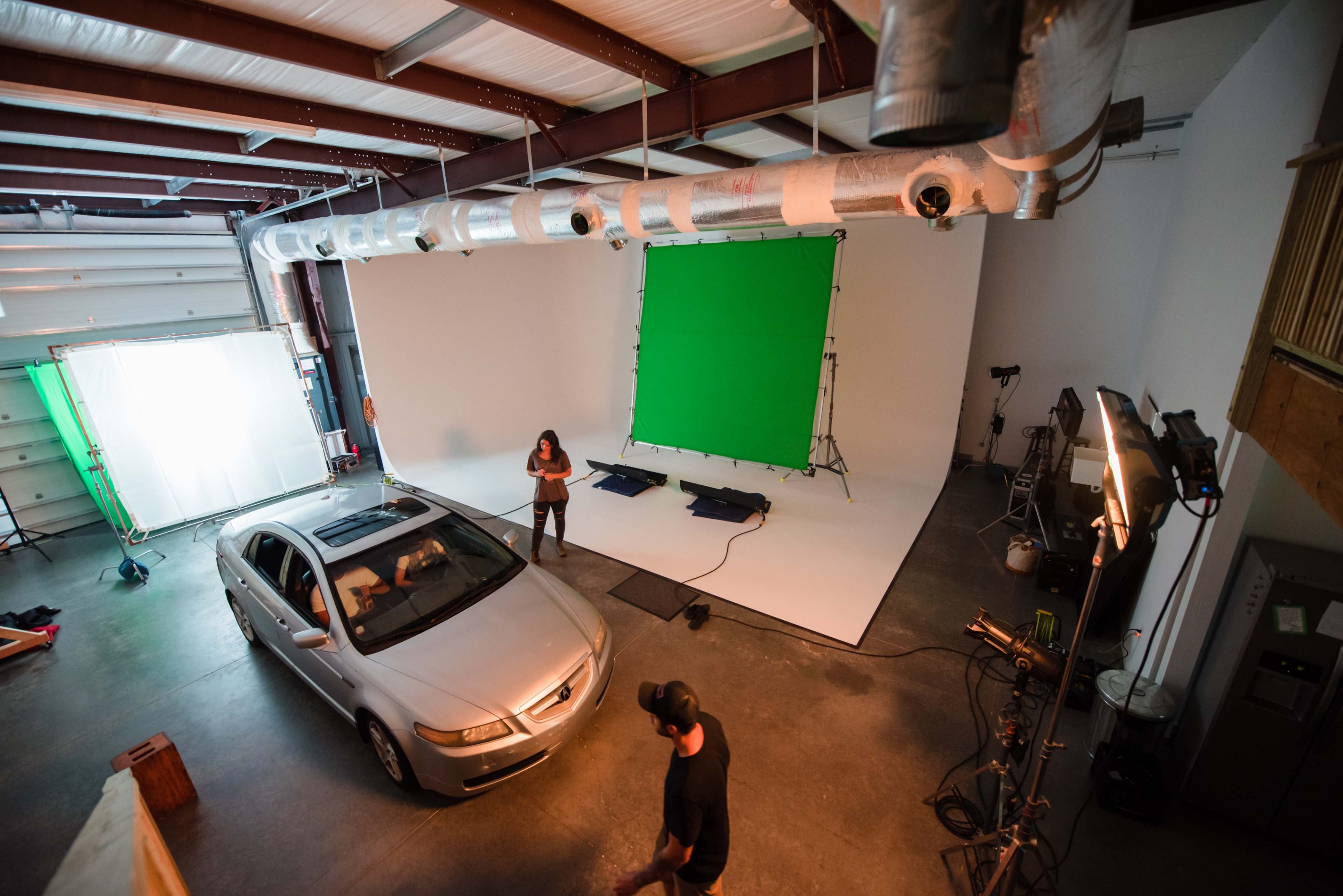 A car is positioned on a soundstage with green screens and lighting equipment set up for a photo or video shoot.