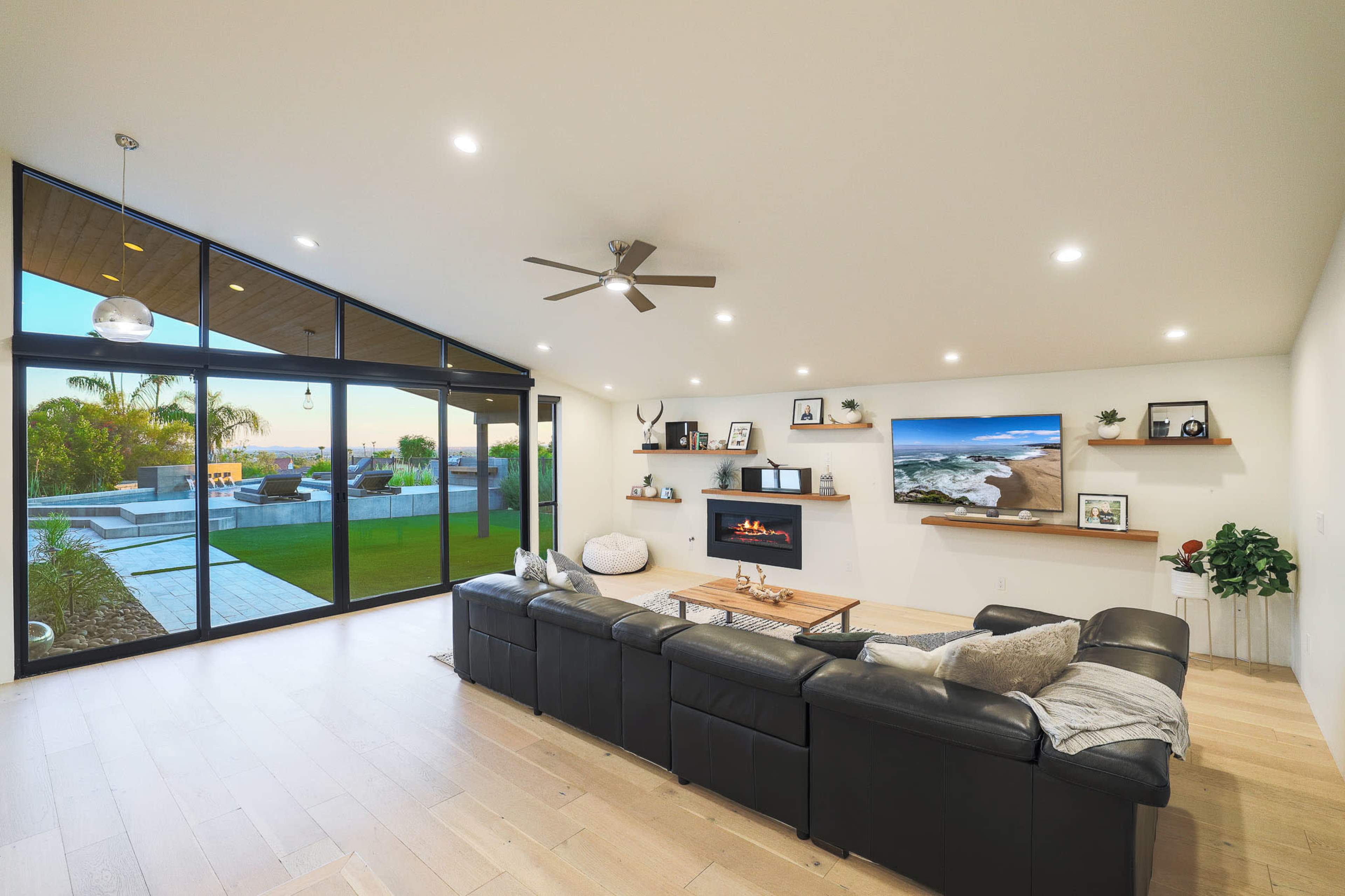 The living room features a large sectional sofa facing a modern television and a fireplace, with large glass doors opening to a backyard.