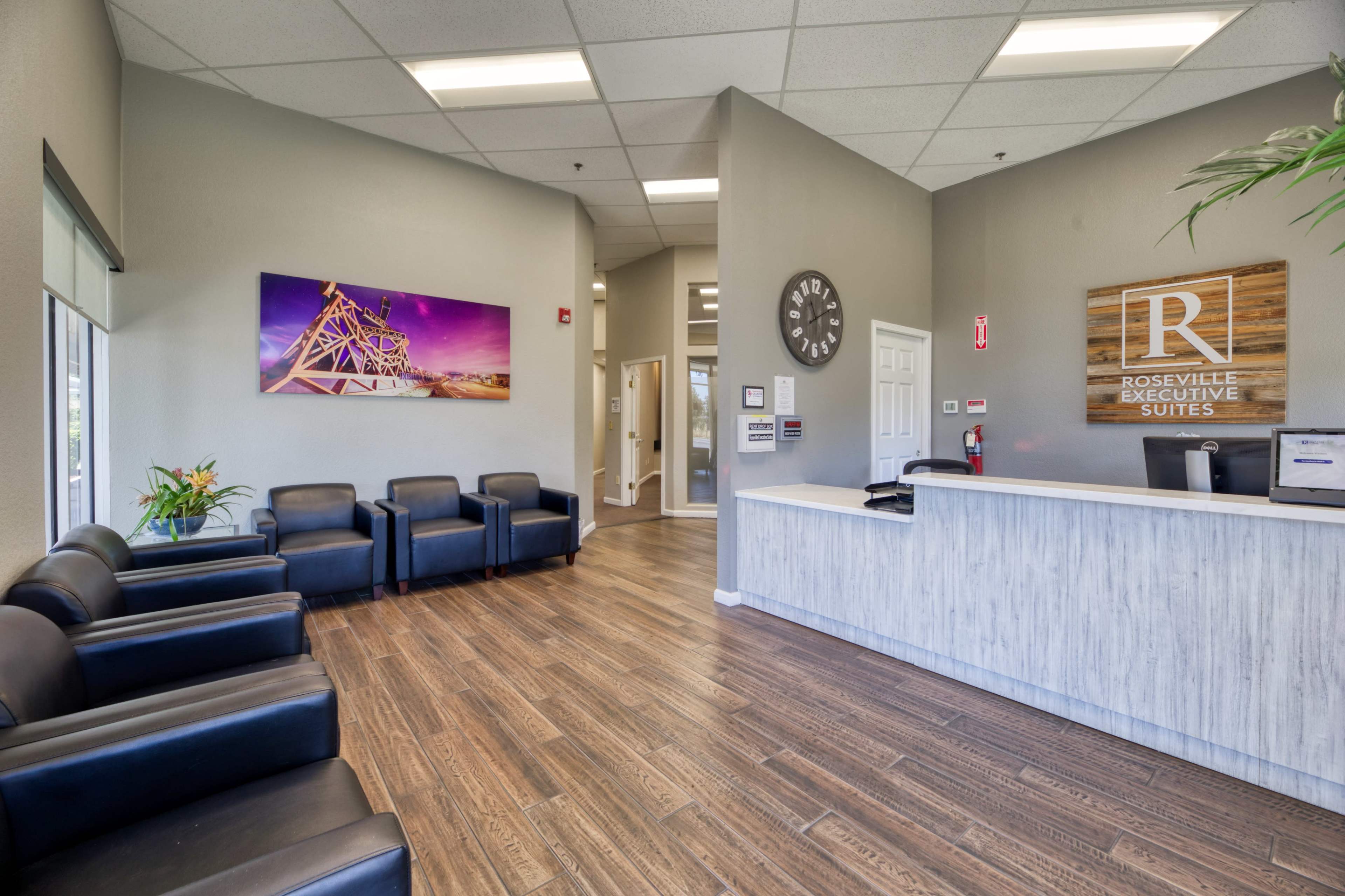 The image depicts a modern reception area with black leather chairs, a front desk, and a wall featuring a colorful artwork in a well-lit environment.