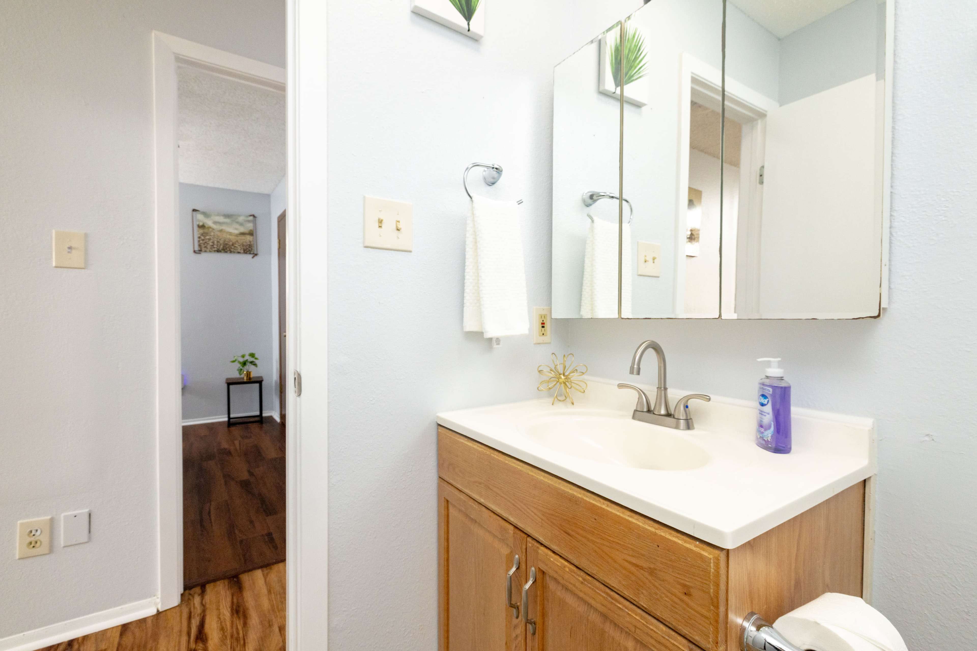 The image shows a bathroom with a single sink, a mirror above it, and a doorway leading to another room.
