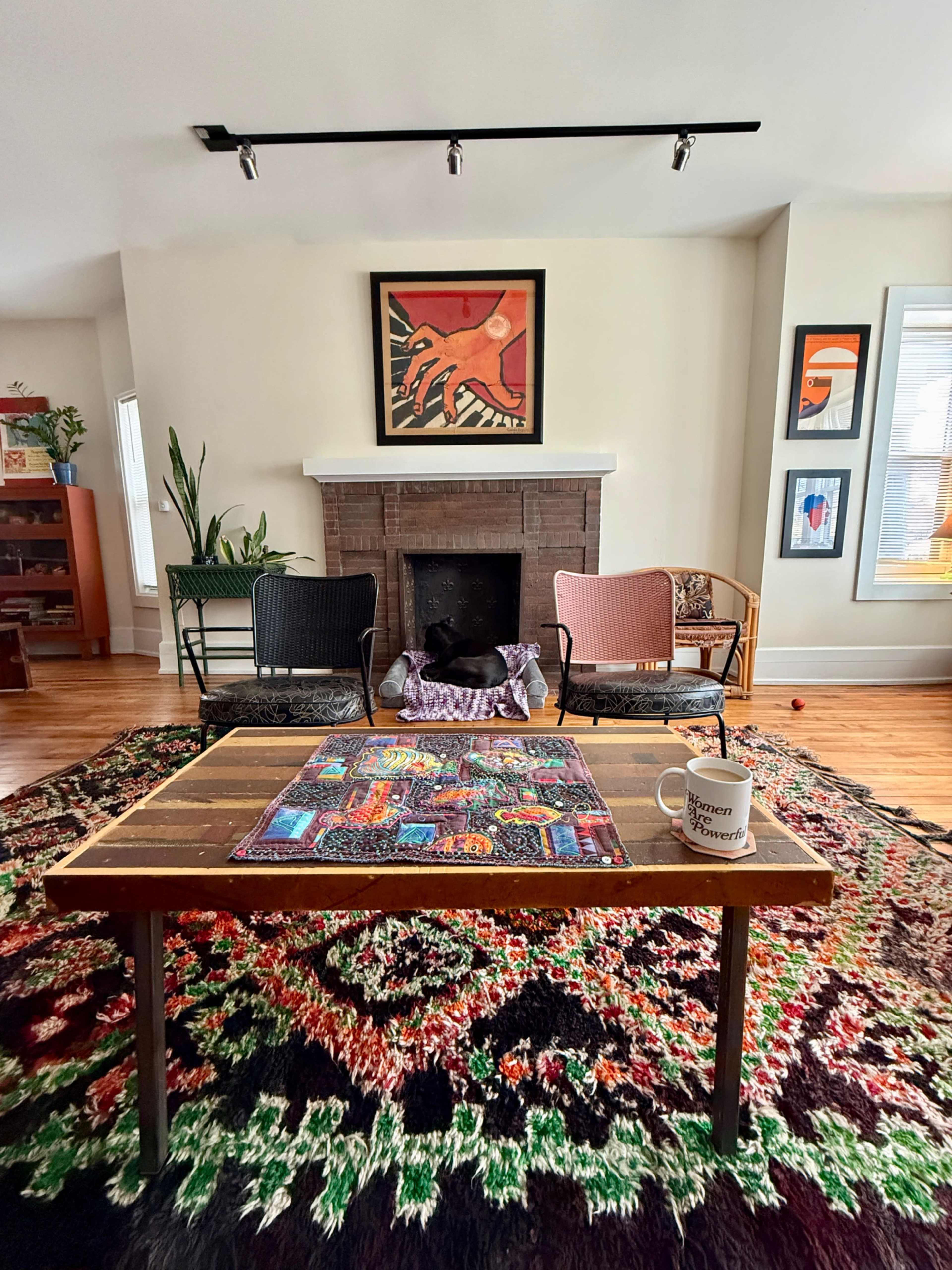 A cozy living room features a wooden coffee table on a patterned rug, flanked by two chairs and decorated with artwork on the walls.
