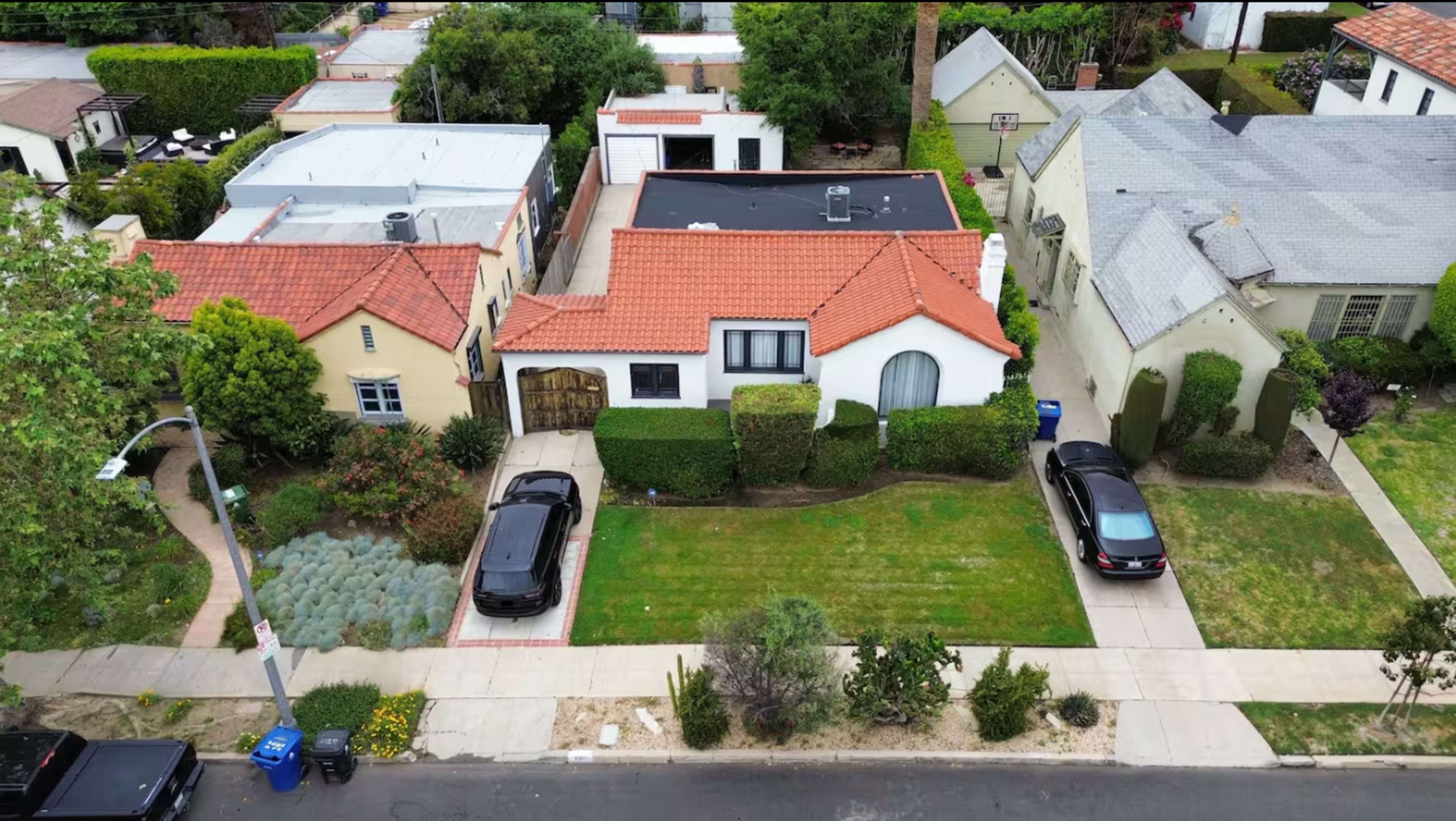 The image shows an aerial view of several houses featuring various architectural styles, with well-maintained lawns and parked cars in the driveways.