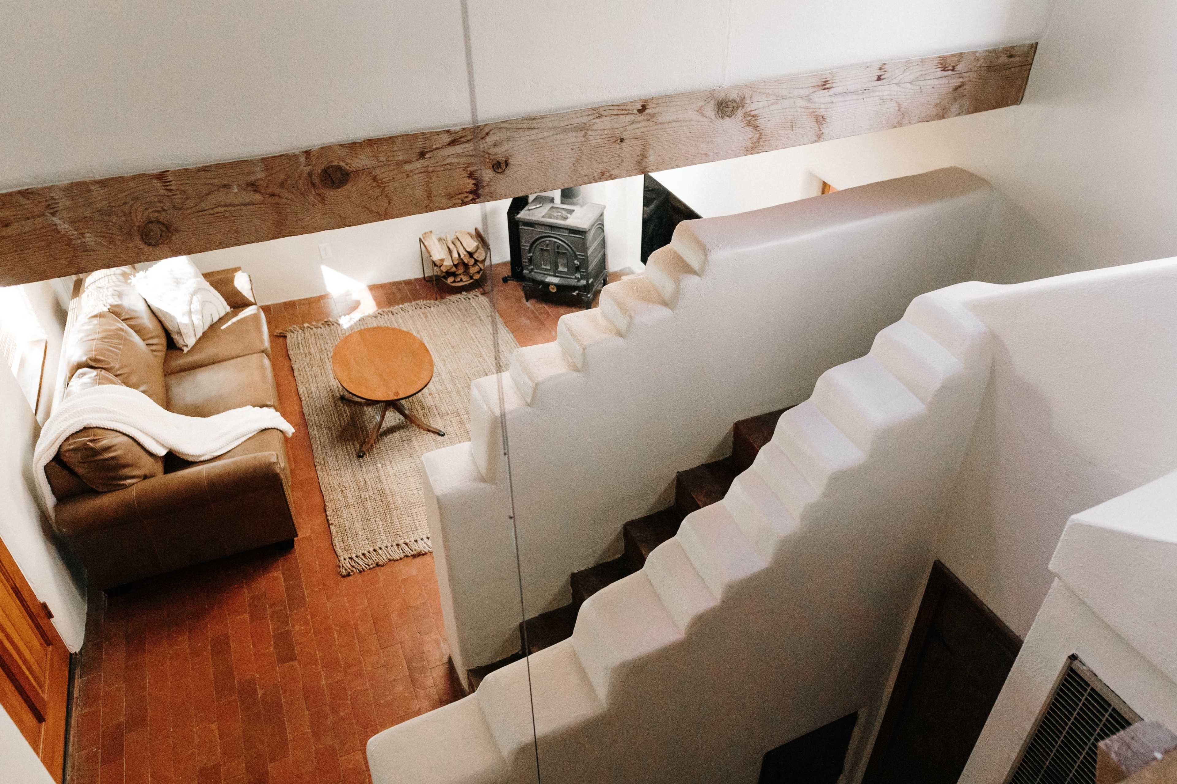 A staircase leading down to a living area with a brown sofa, circular wooden coffee table, and a rustic rug.
