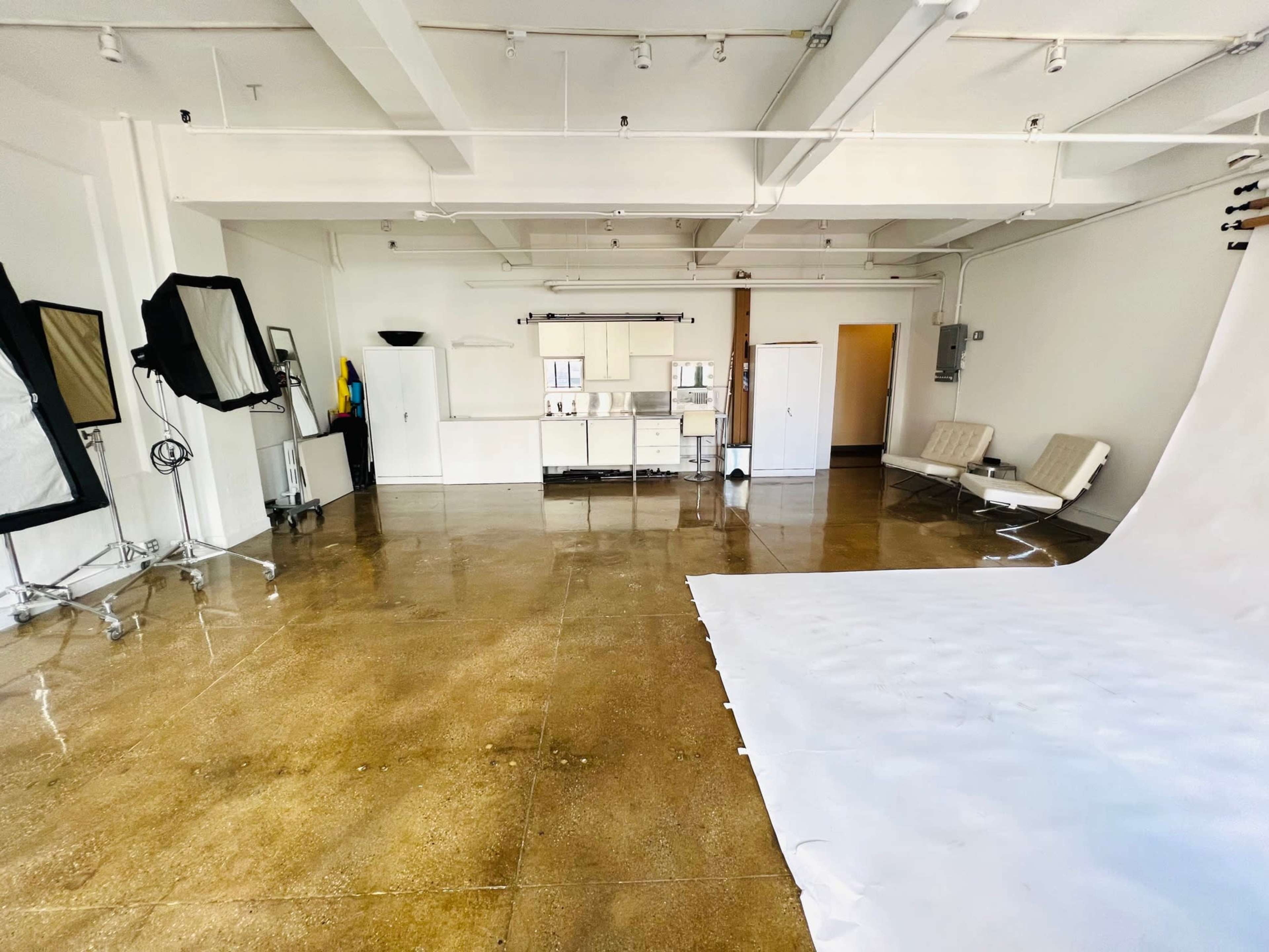 The image shows a spacious photography studio with a white backdrop, shiny concrete floors, and two large mirrors on stands in a minimalist setting.