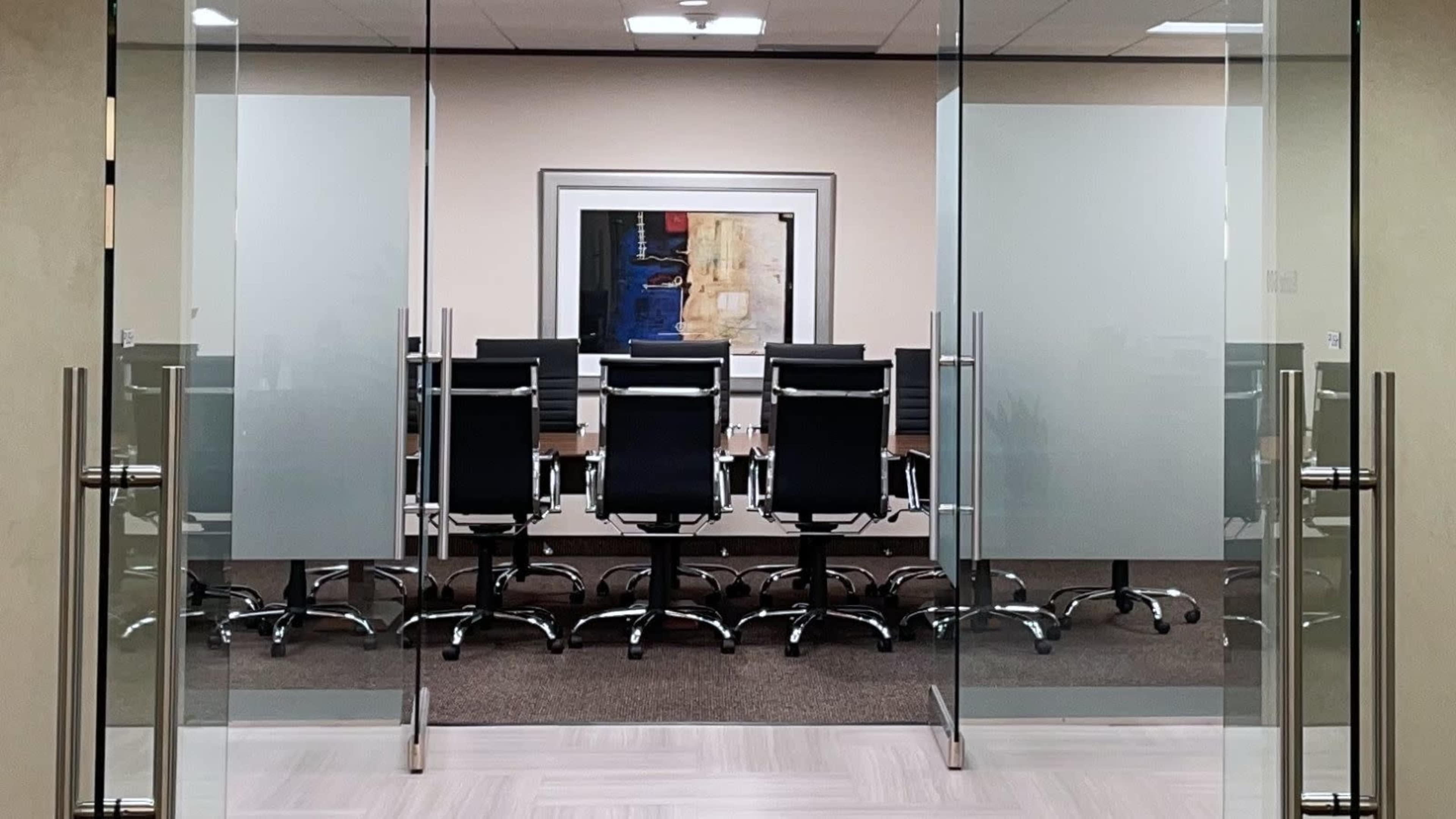A modern conference room with a long table and black rolling chairs is visible through glass doors.