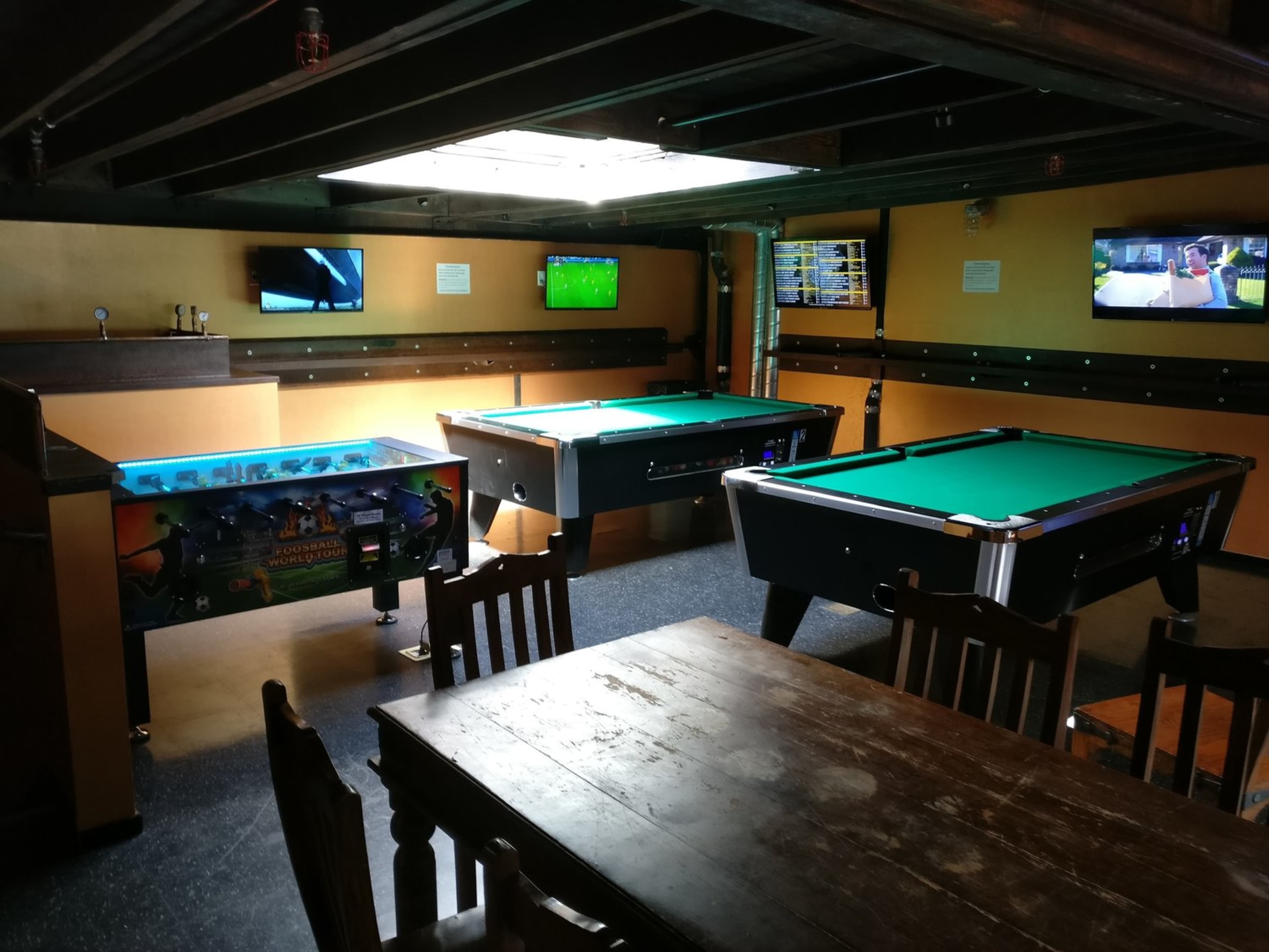 A game room featuring two pool tables, a pinball machine, multiple televisions, and a wooden dining table.
