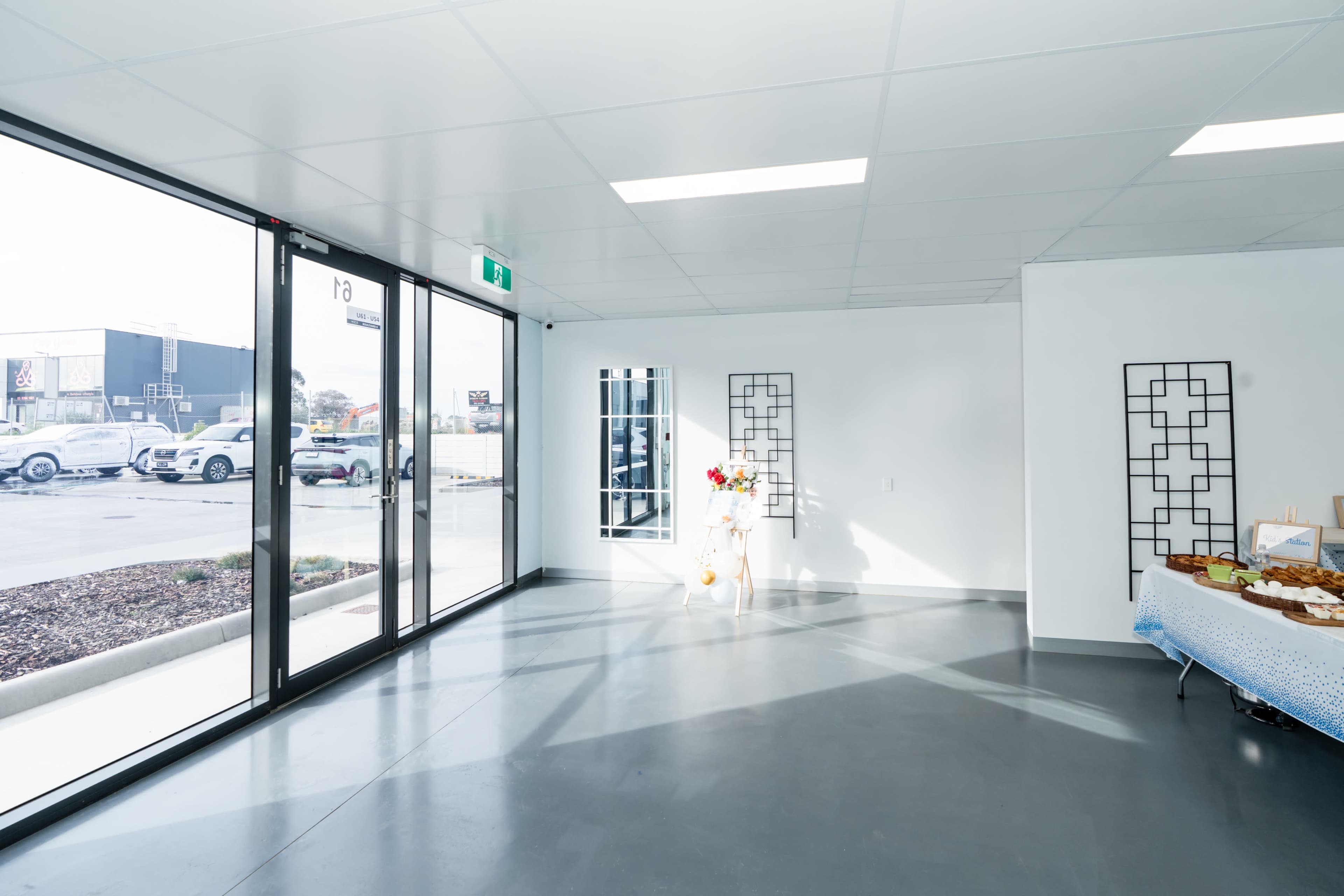 The image shows a bright, empty room with large glass doors, a few decorative wall features, and a table covered with a blue tablecloth.