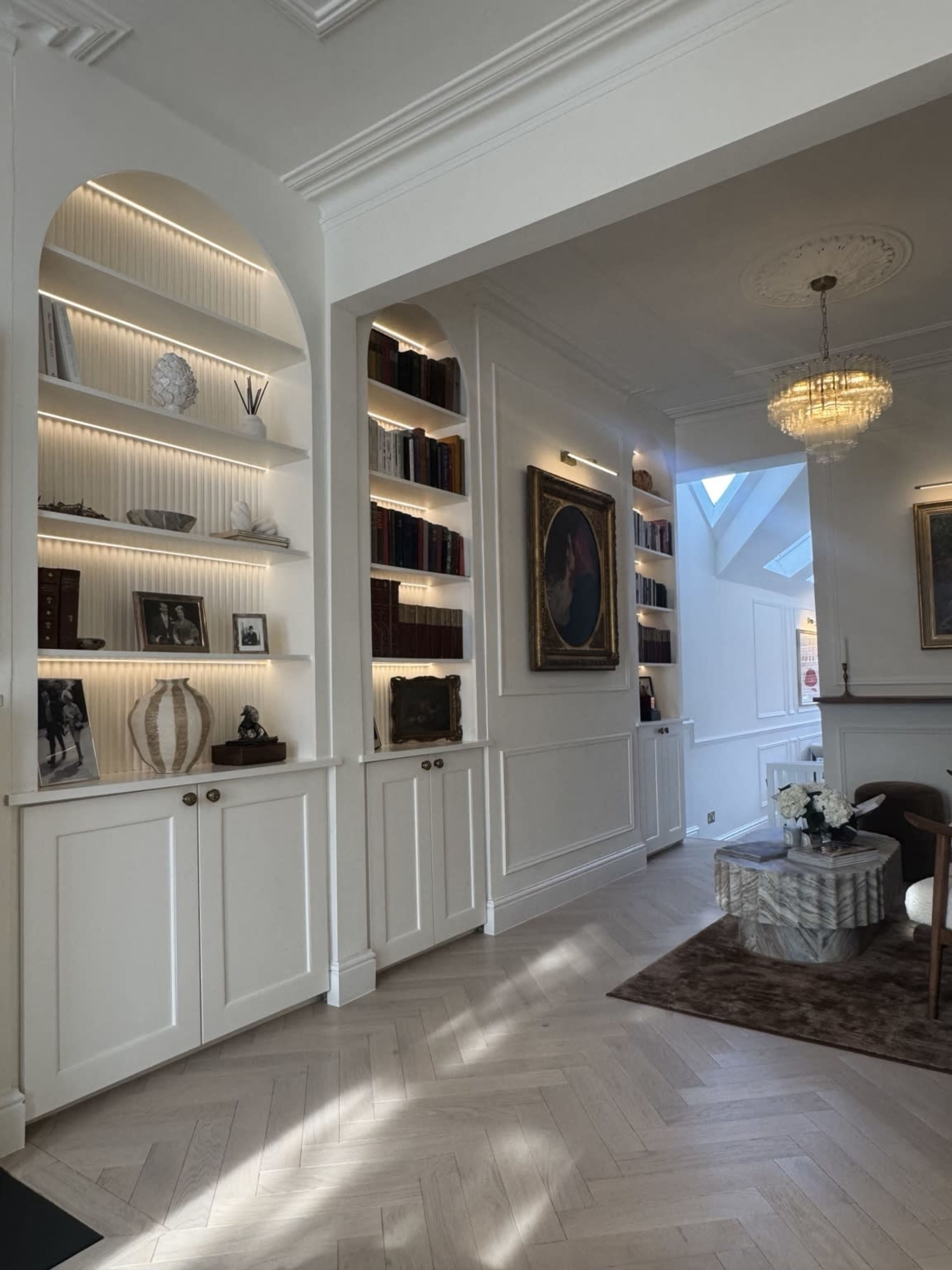 The image shows a stylish interior of a living space with white shelving units, decorative items, and a chandelier.