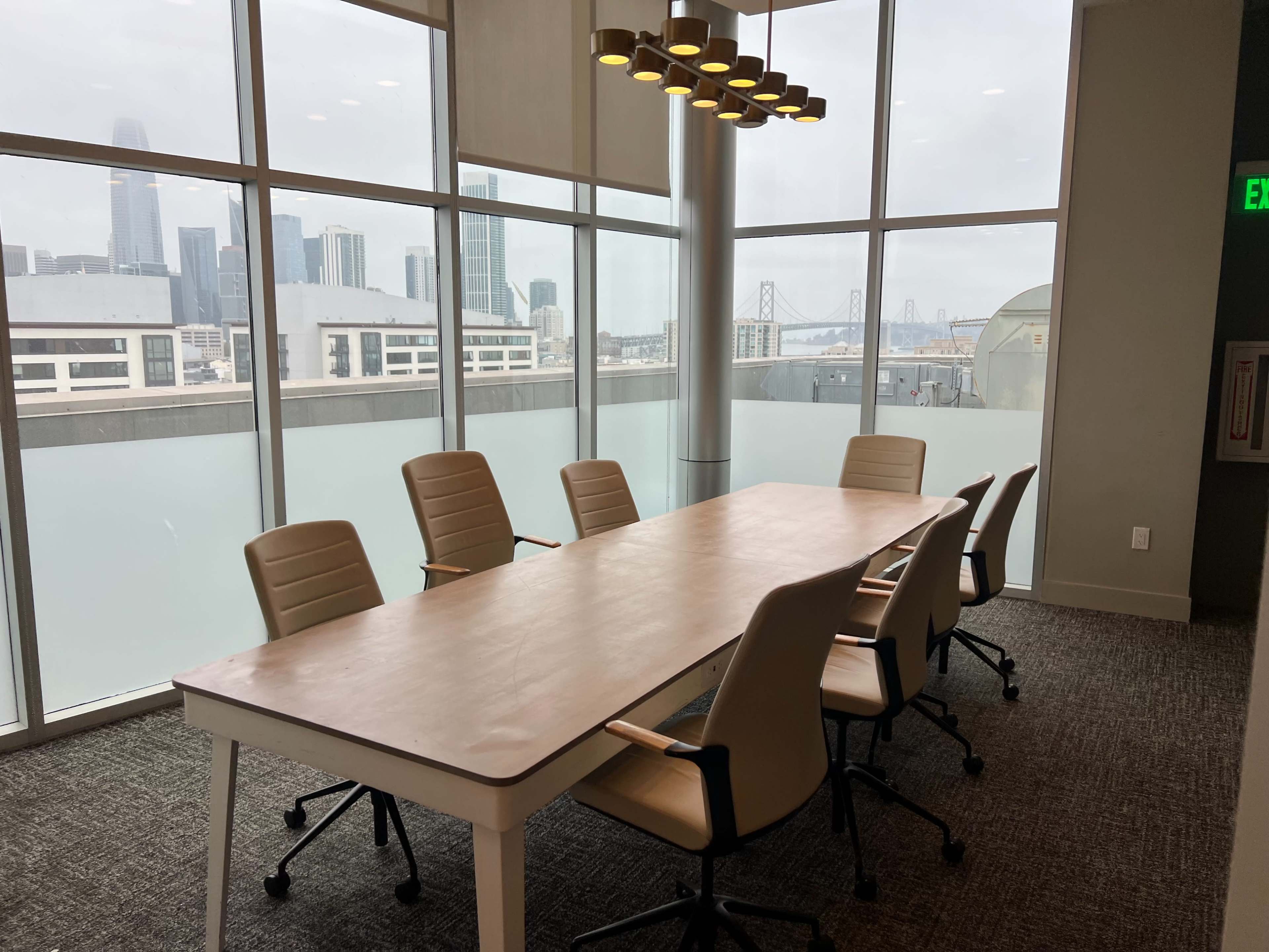 A modern meeting room with a long table and several chairs overlooks a city skyline through large windows.