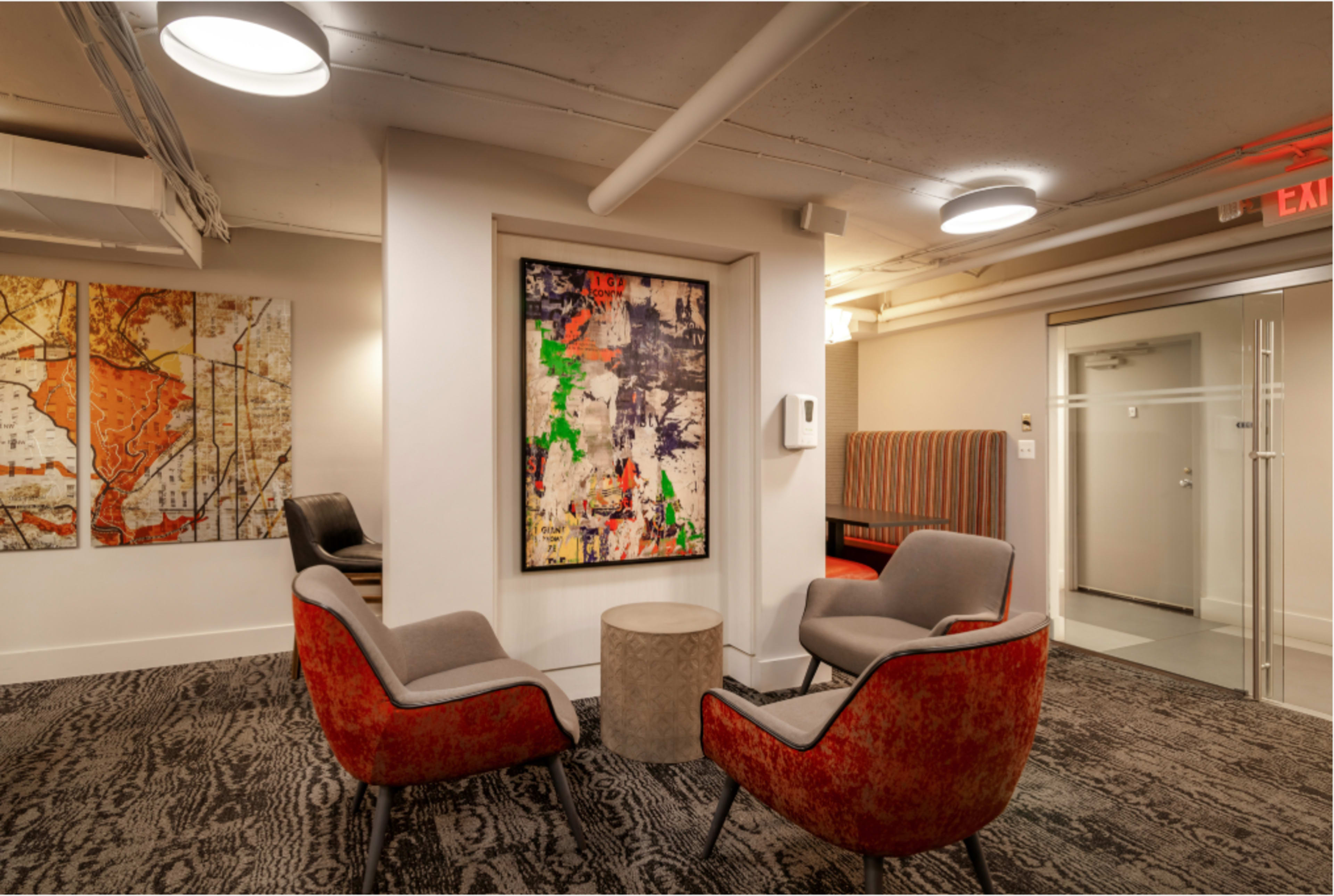 The image depicts a modern lounge area featuring two red and gray chairs, a round coffee table, and an abstract painting on the wall, complemented by a map-themed artwork nearby.