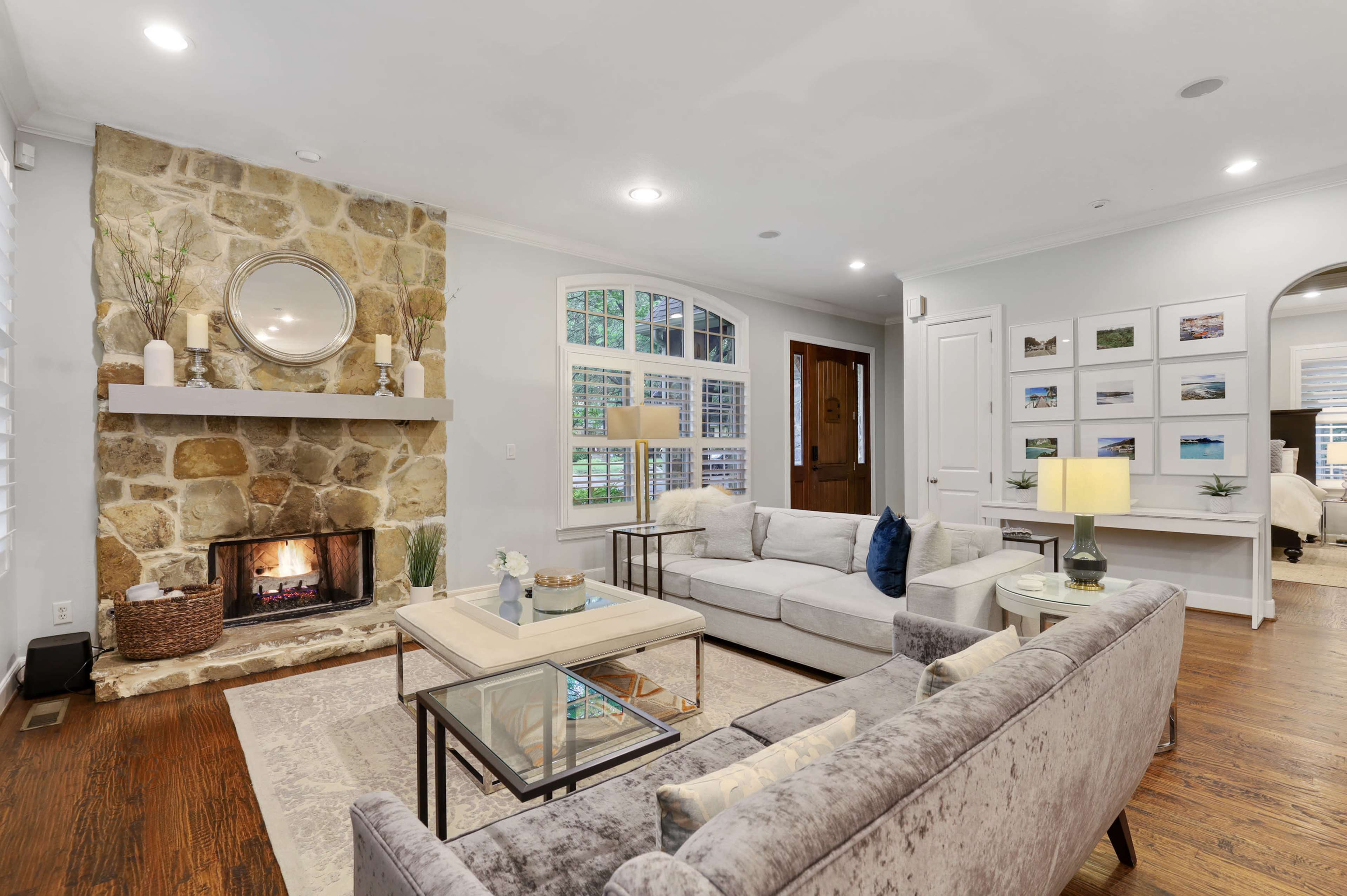 A well-lit living room with a stone fireplace, a gray sofa, and a coffee table arranged on a hardwood floor.