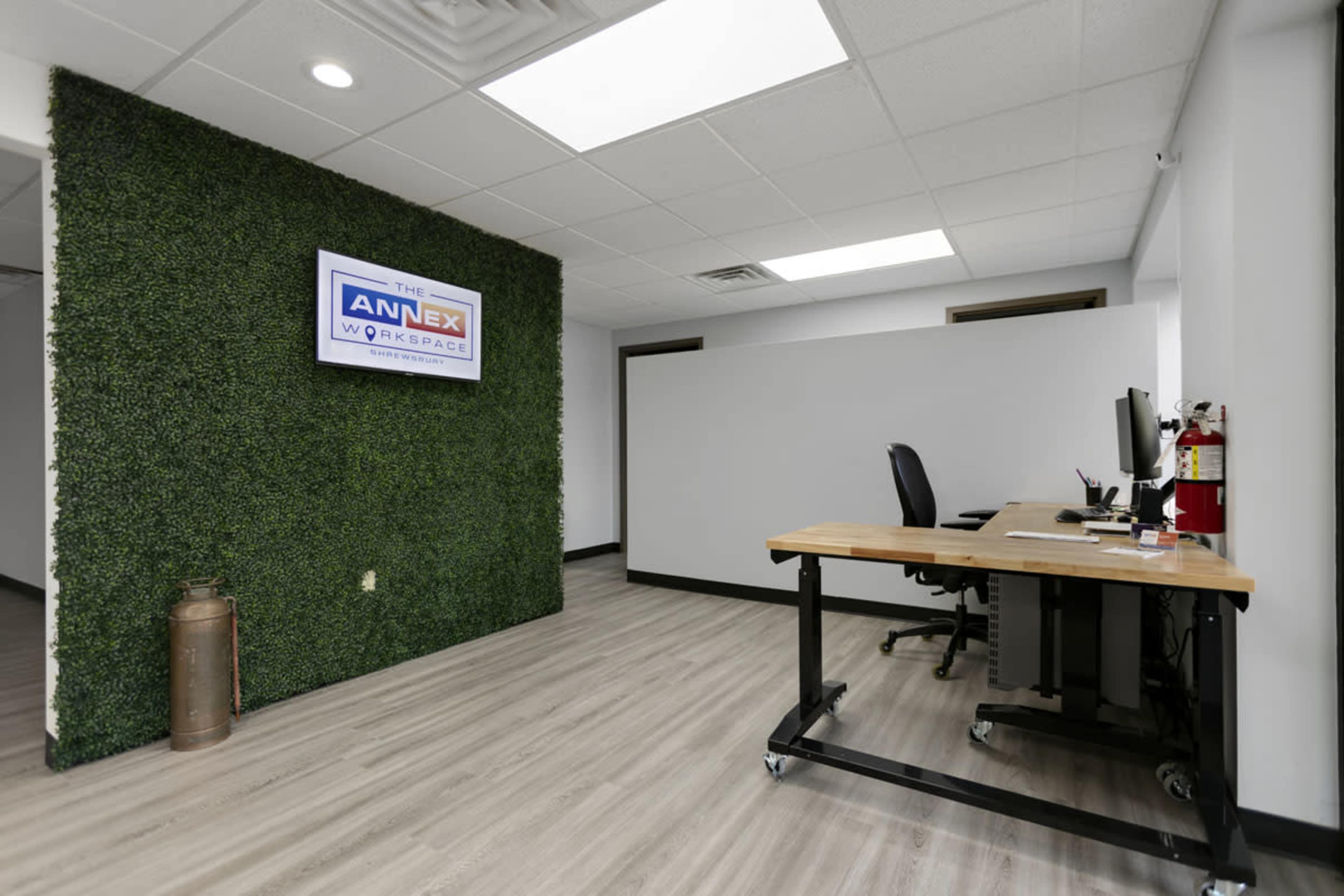 A modern workspace featuring a green wall, a desk with a computer, and a fire extinguisher mounted on the wall.