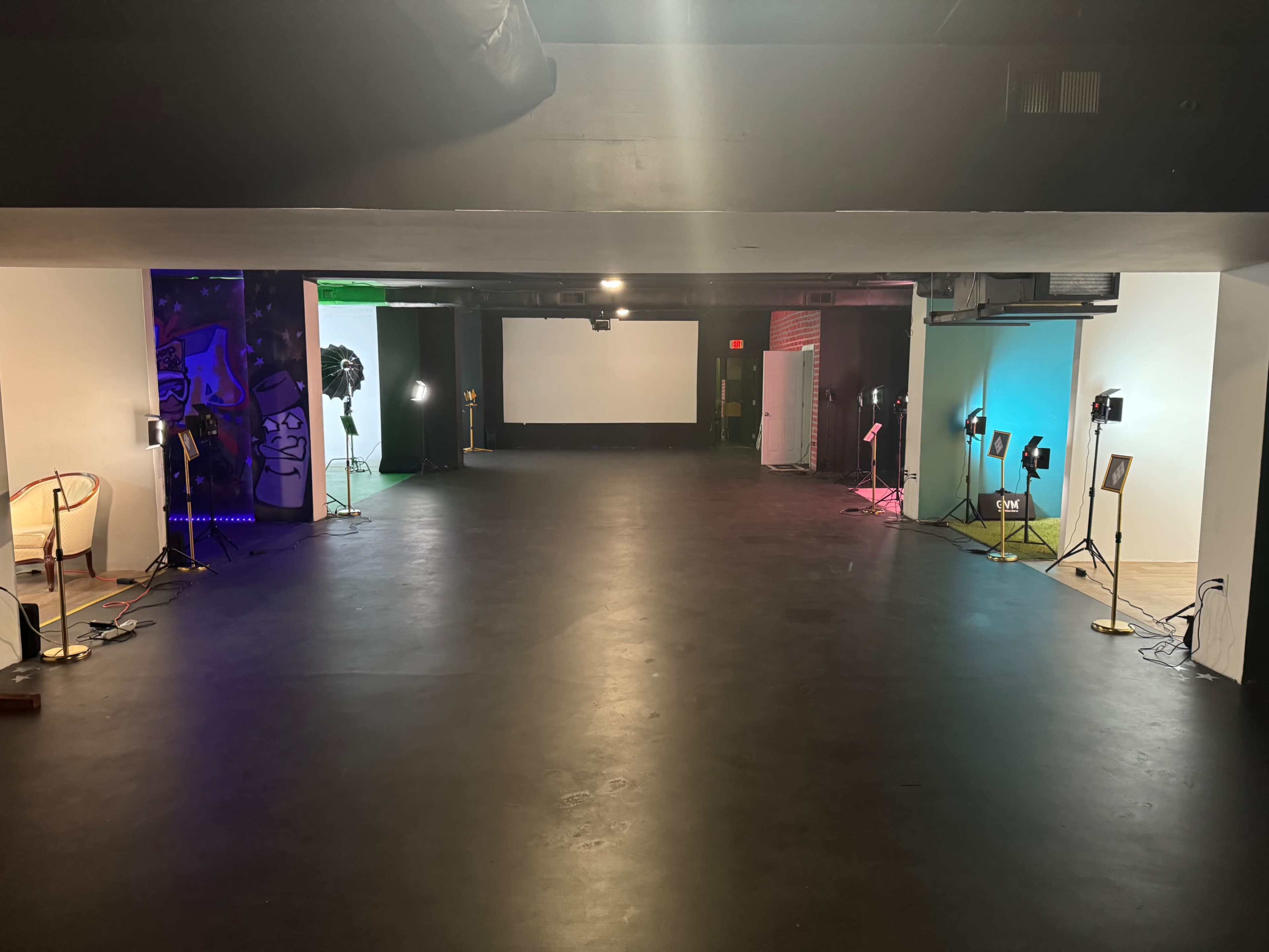The image shows an empty indoor space with a large screen at one end and colorful lighting setups along the sides.