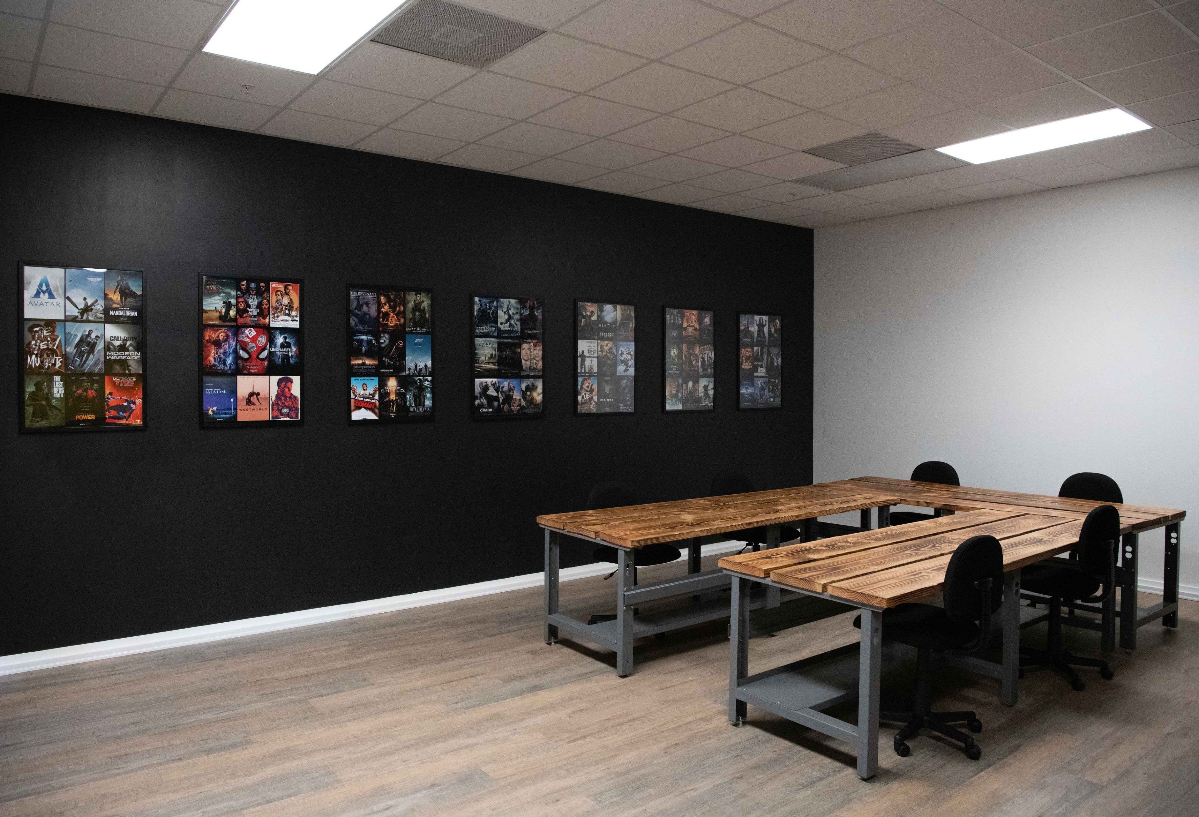 A meeting room features a wooden table surrounded by chairs, with a gallery of framed images displayed on the black wall.
