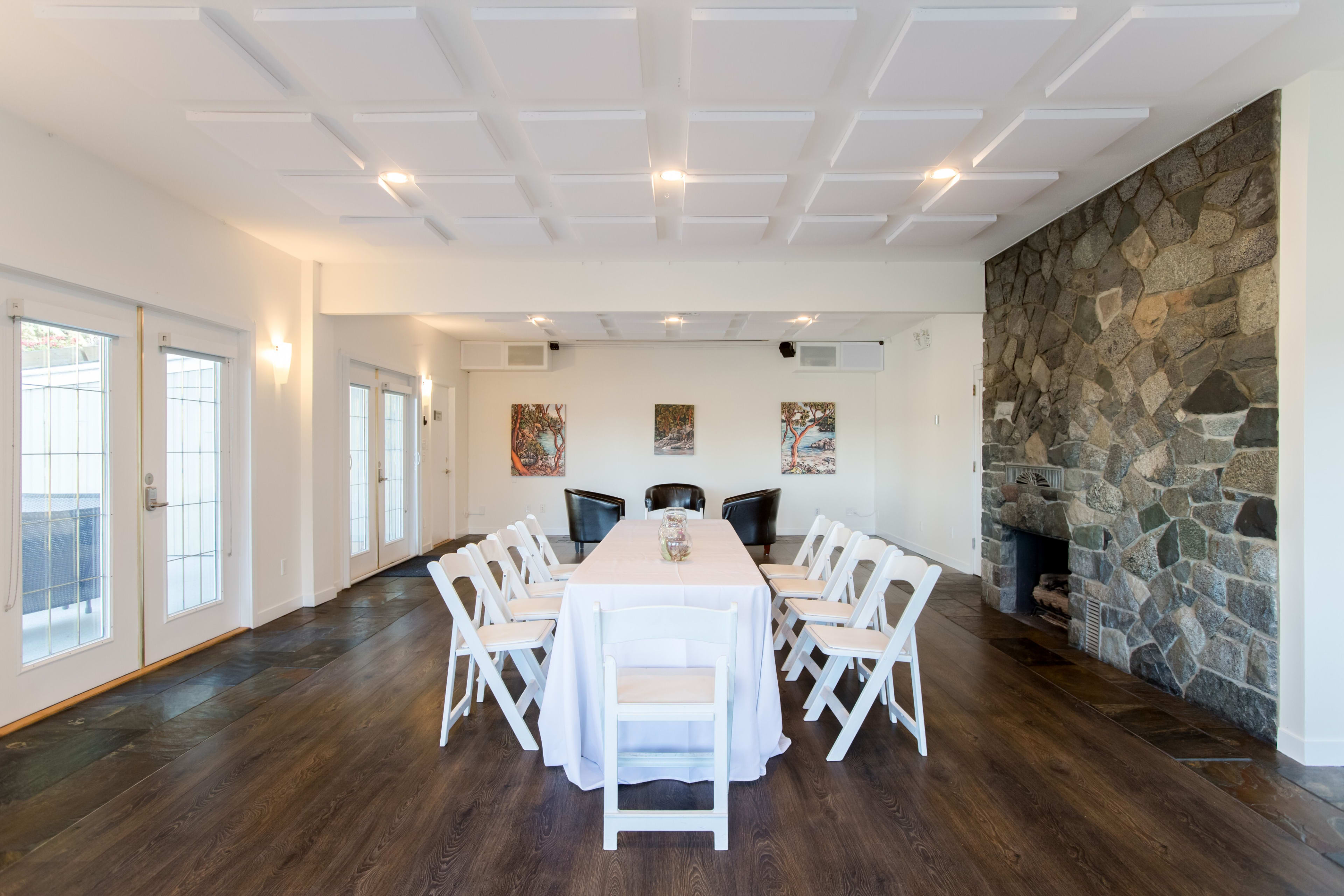 A conference room features a long table with white chairs, stone walls, and artwork on display.