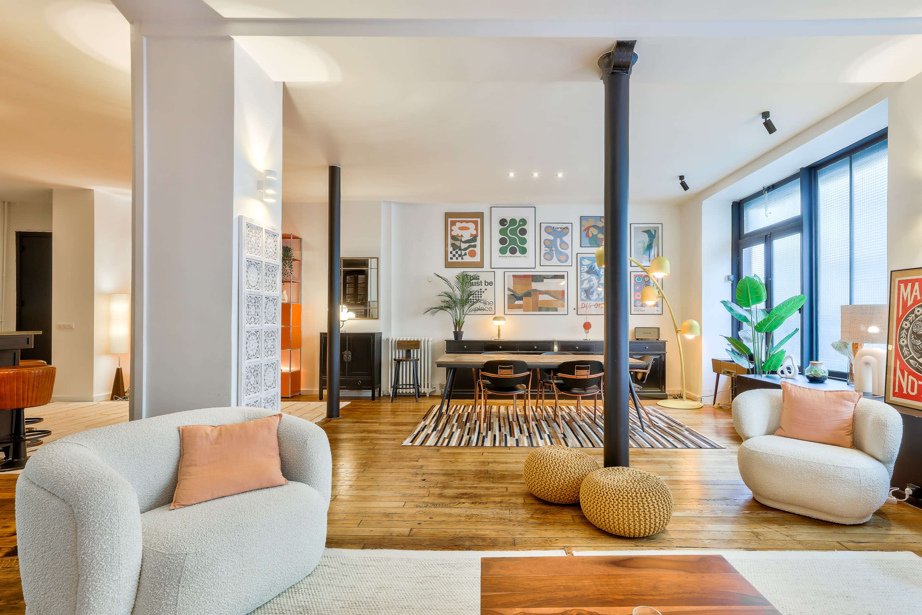 A spacious living area features modern furniture, artwork on the walls, and large windows allowing natural light.