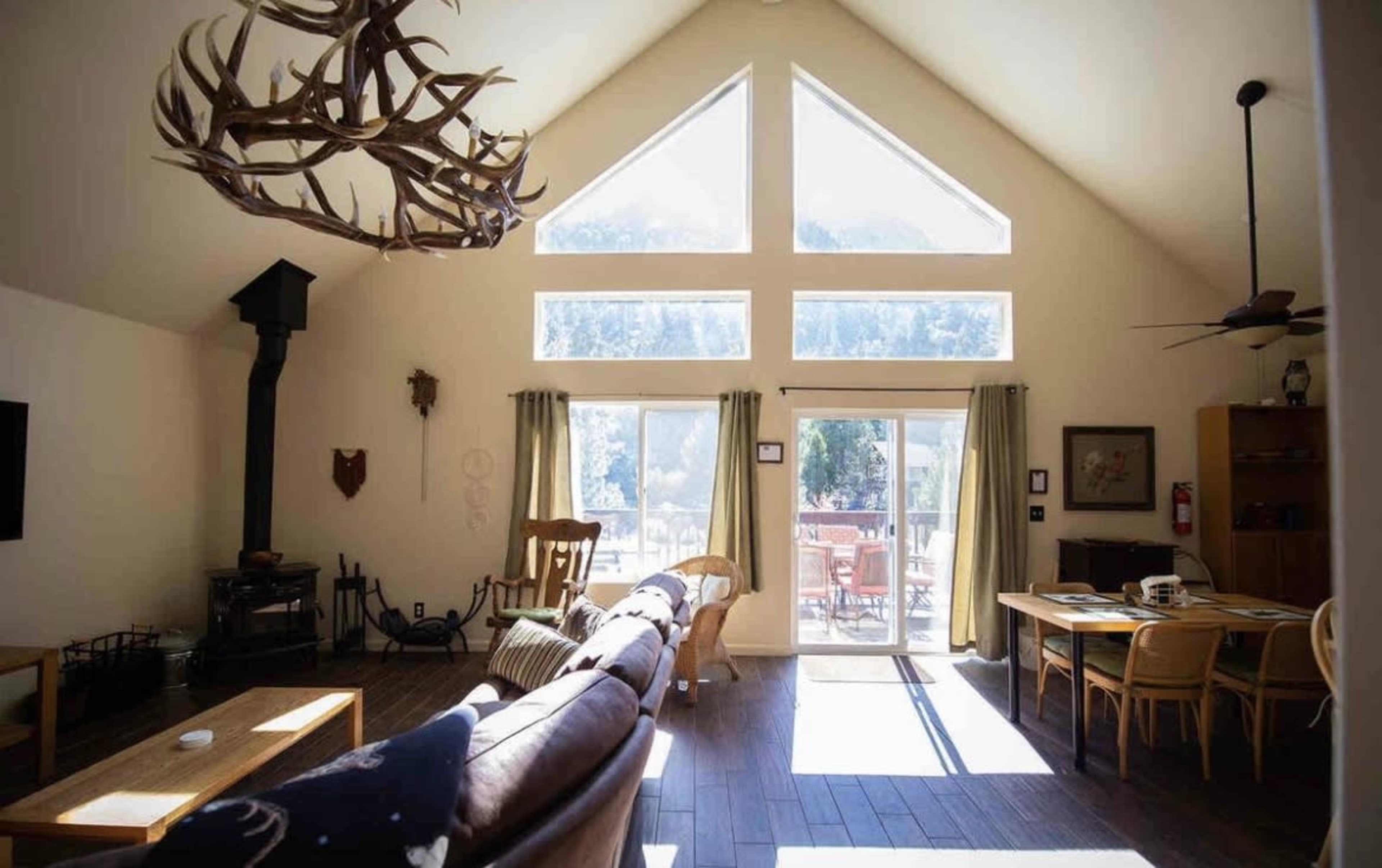 A spacious living room features high ceilings, large windows, and a central dining table with views of the outdoors.