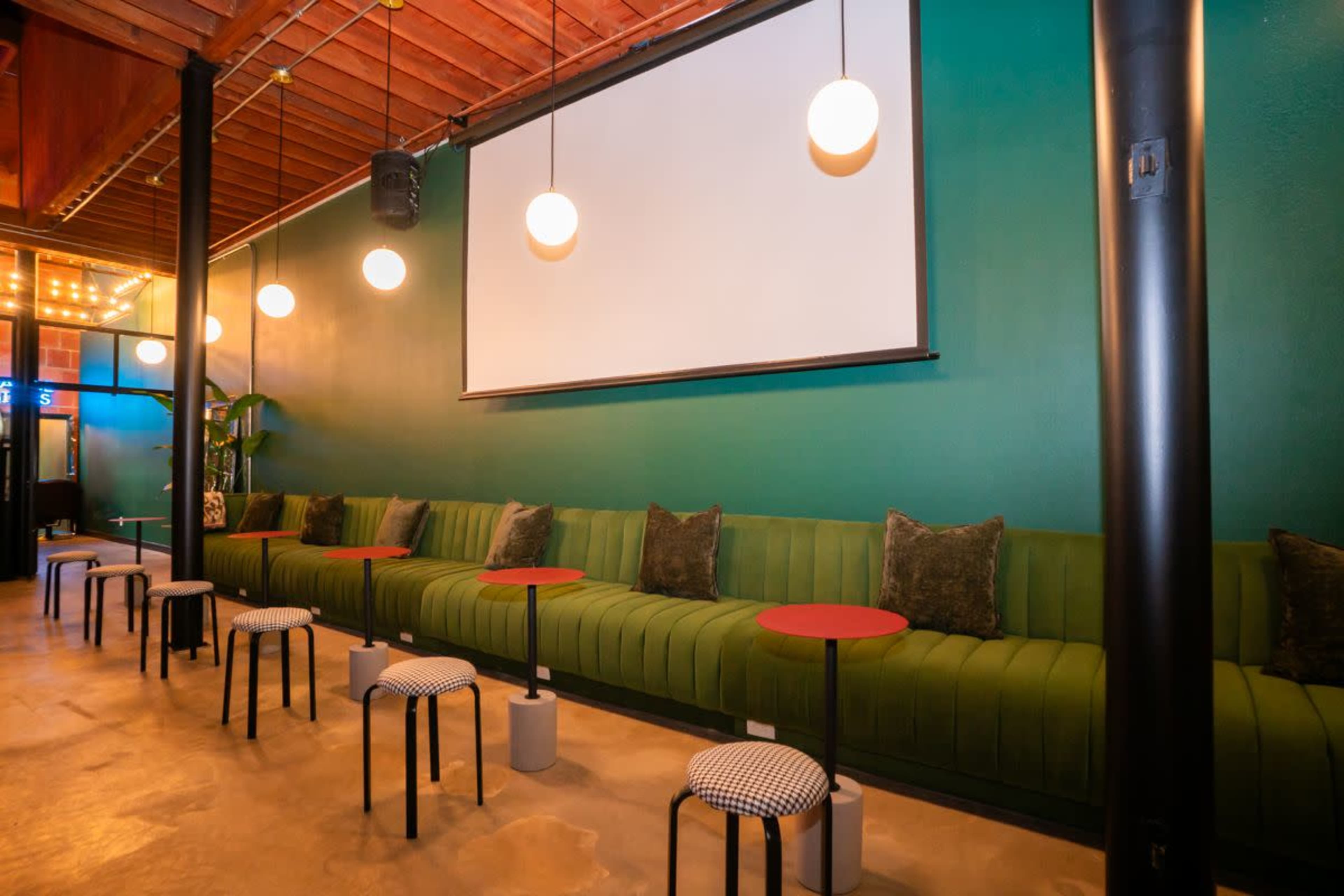 The image features a modern interior with a green upholstered seating area, round tables, and hanging light fixtures against a textured wall.