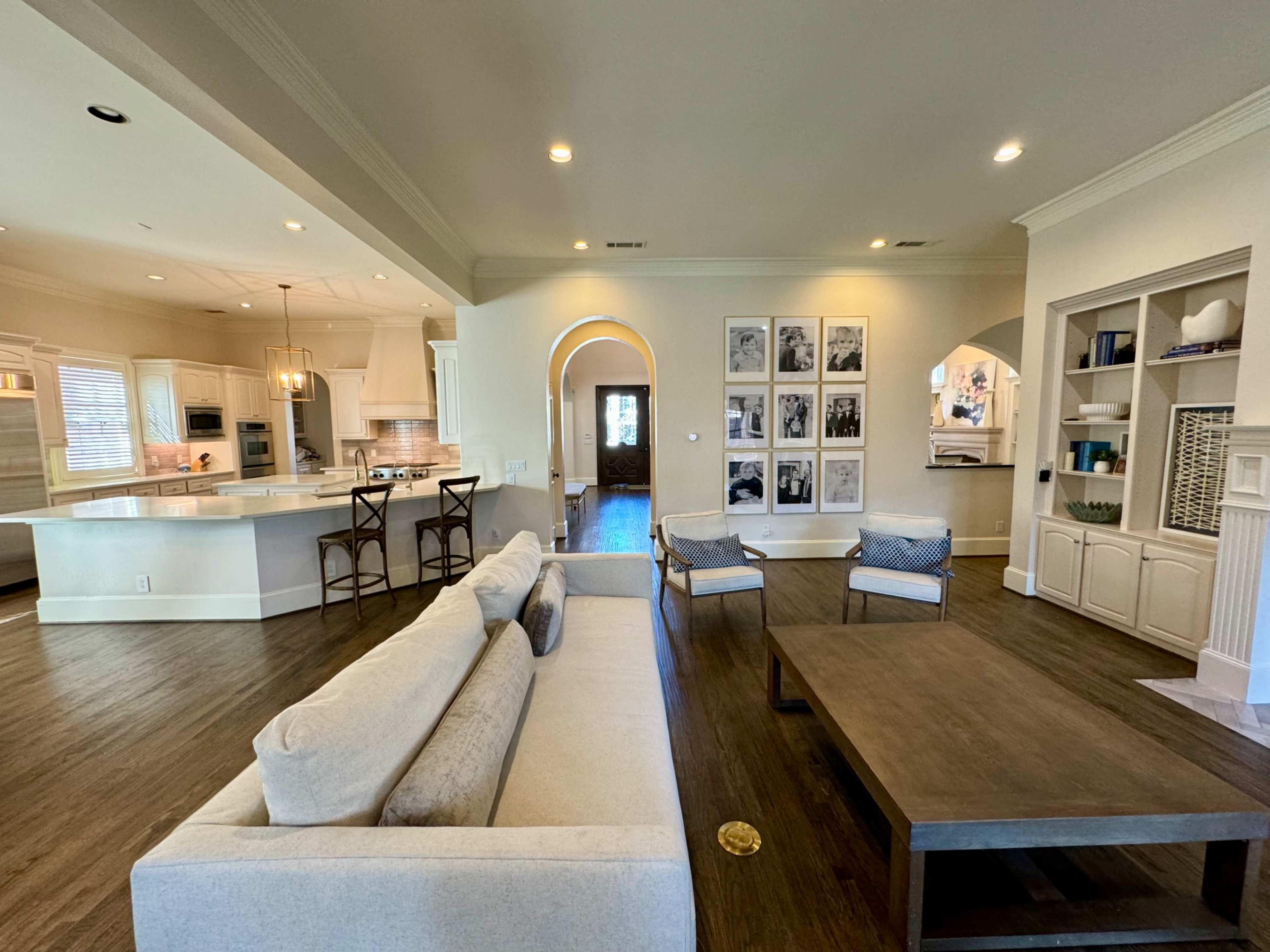 A spacious living room with a light-colored sofa, a wooden coffee table, and a series of black and white framed photos on the wall.