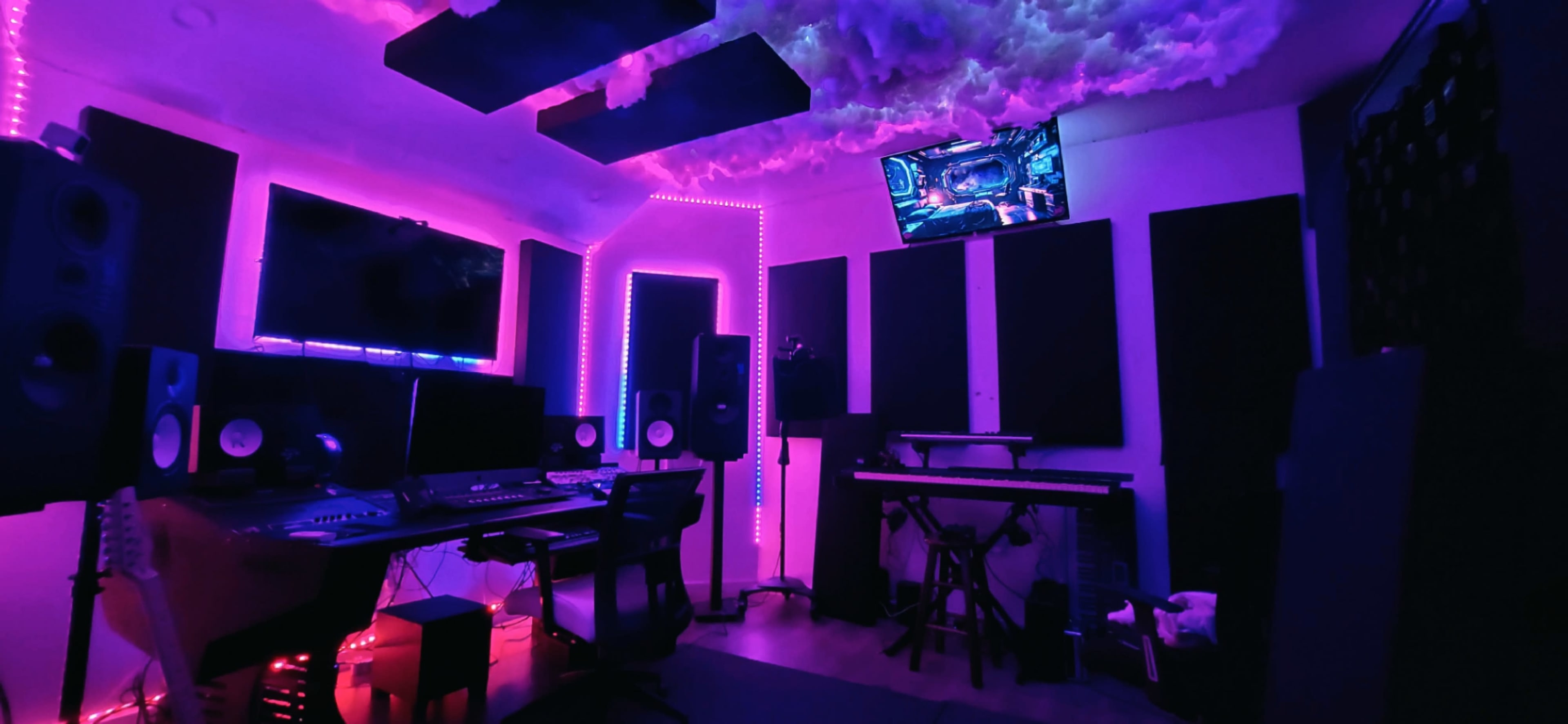 A music studio with computer desks, monitors, musical equipment, and ambient lighting in shades of purple and pink.