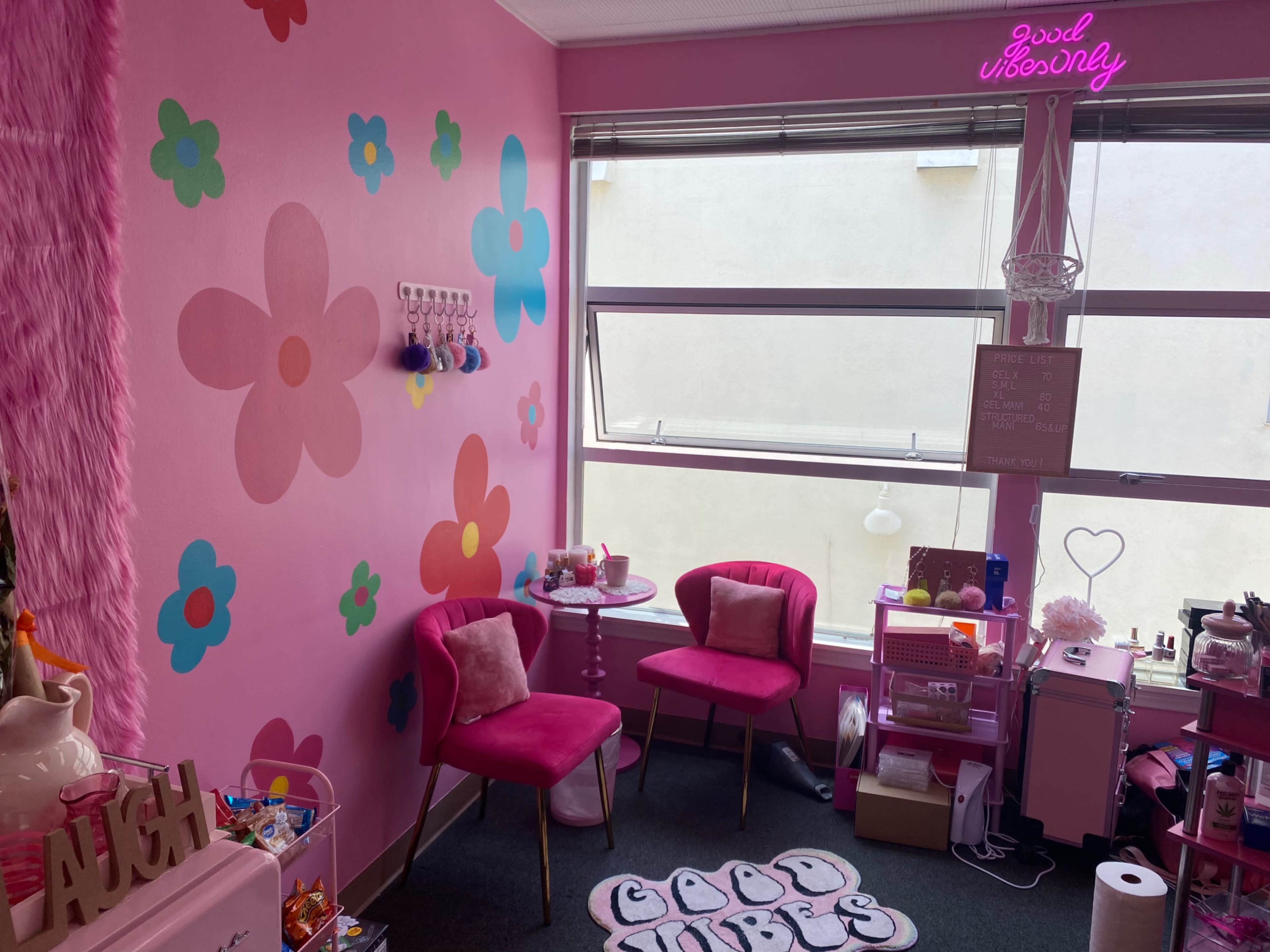 The image shows a brightly colored room with pink walls decorated with flower patterns, featuring two pink chairs and a small table under a window.