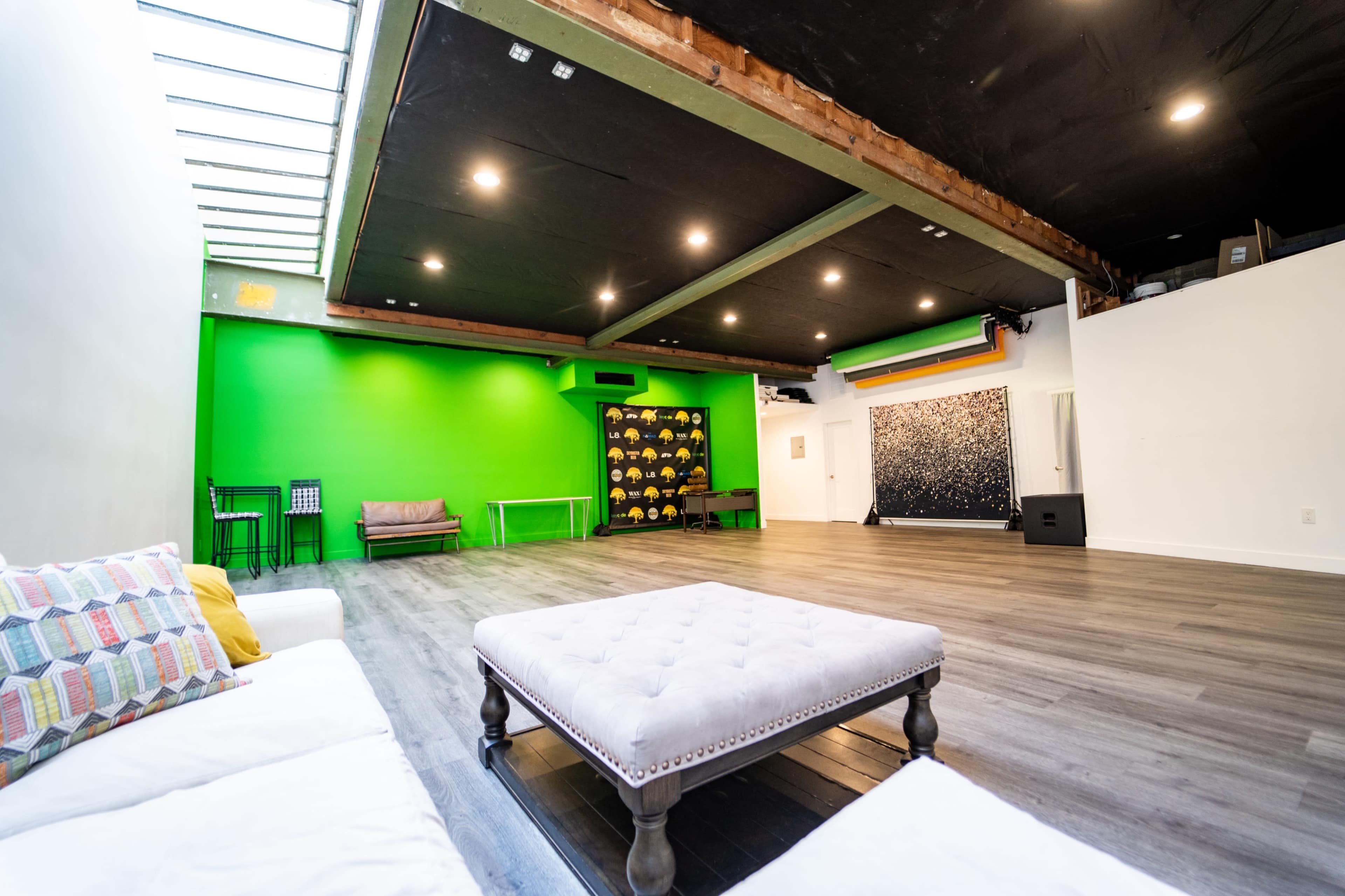 A spacious room featuring a green wall, a tufted coffee table in the center, and a seating area with a couch and chairs along one side.