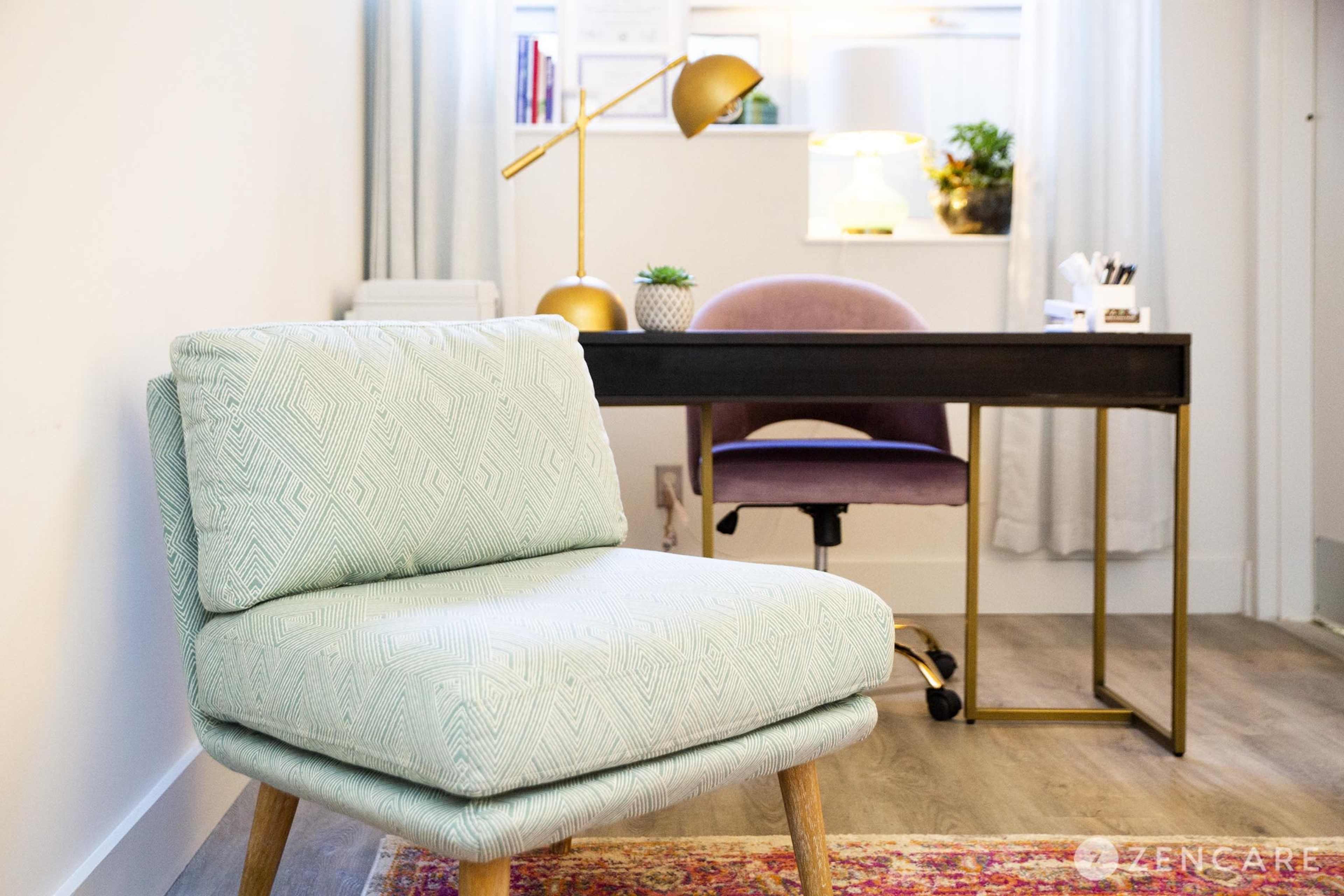 A light blue patterned armchair is positioned in the foreground, with a black desk and a purple office chair visible in the background.