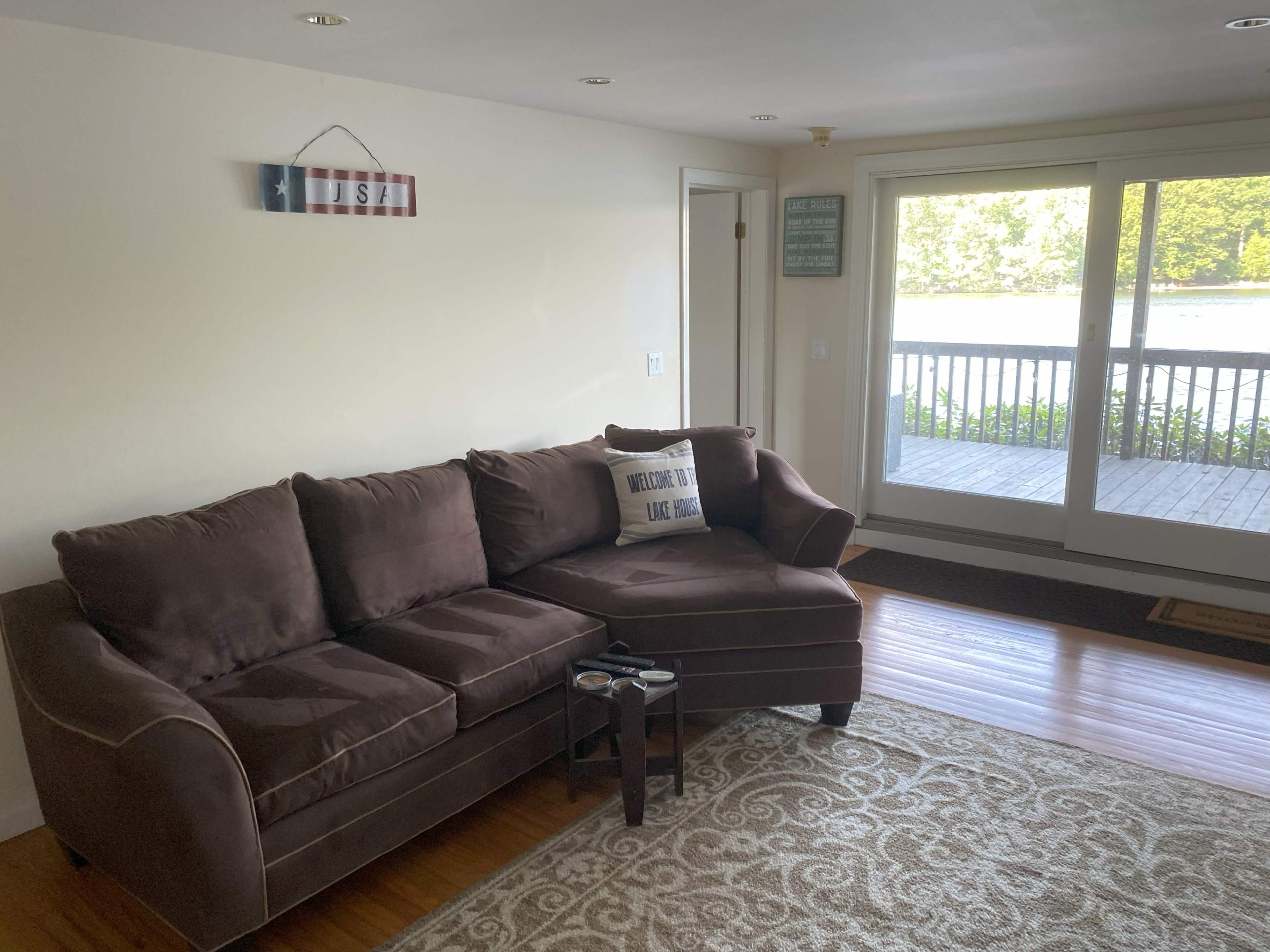 A brown sectional sofa is positioned in a well-lit room with large windows overlooking a deck and a view of the outdoors.