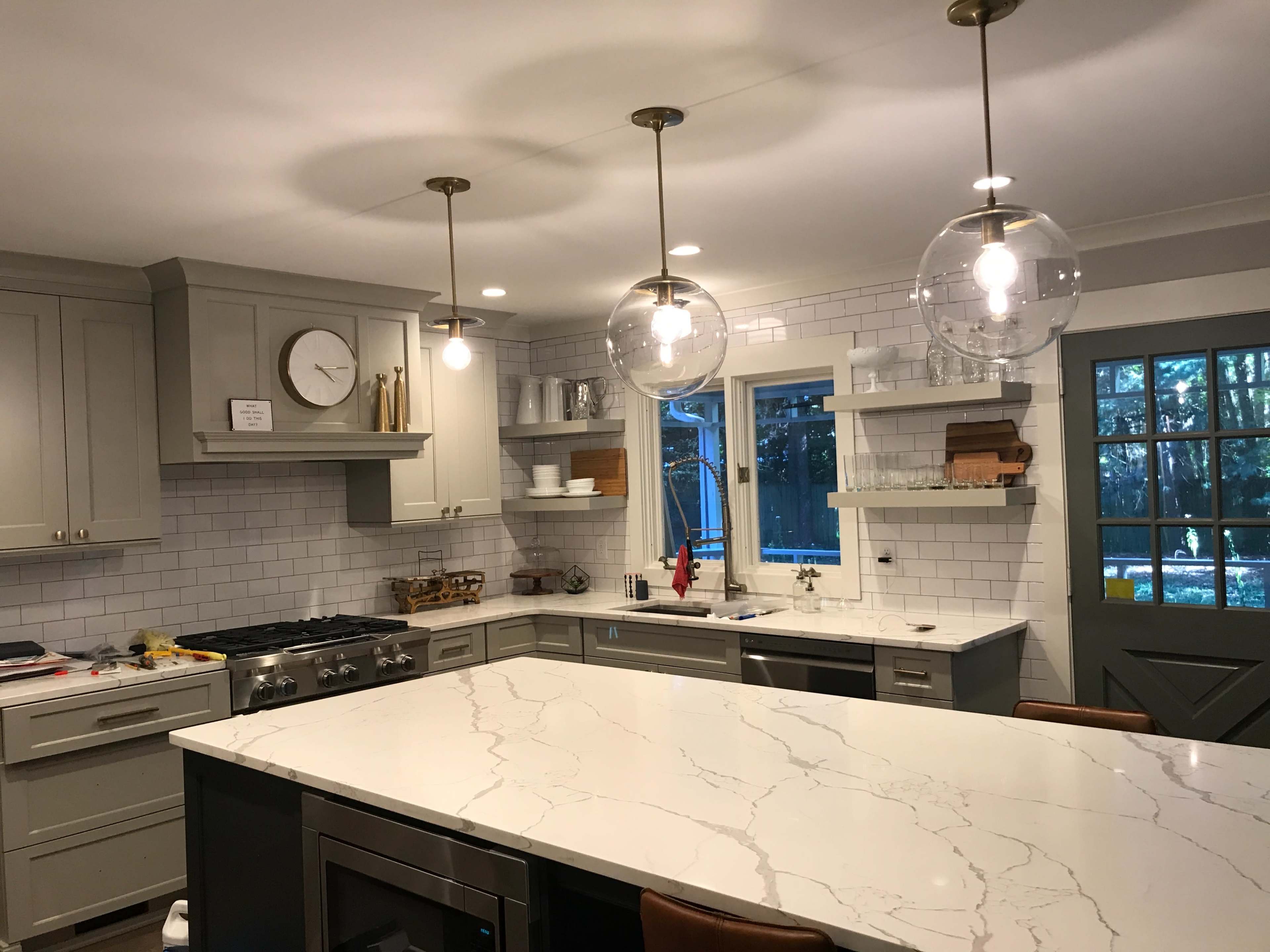 A modern kitchen features a central island with a marble countertop, gray cabinetry, and overhead globe-shaped light fixtures.