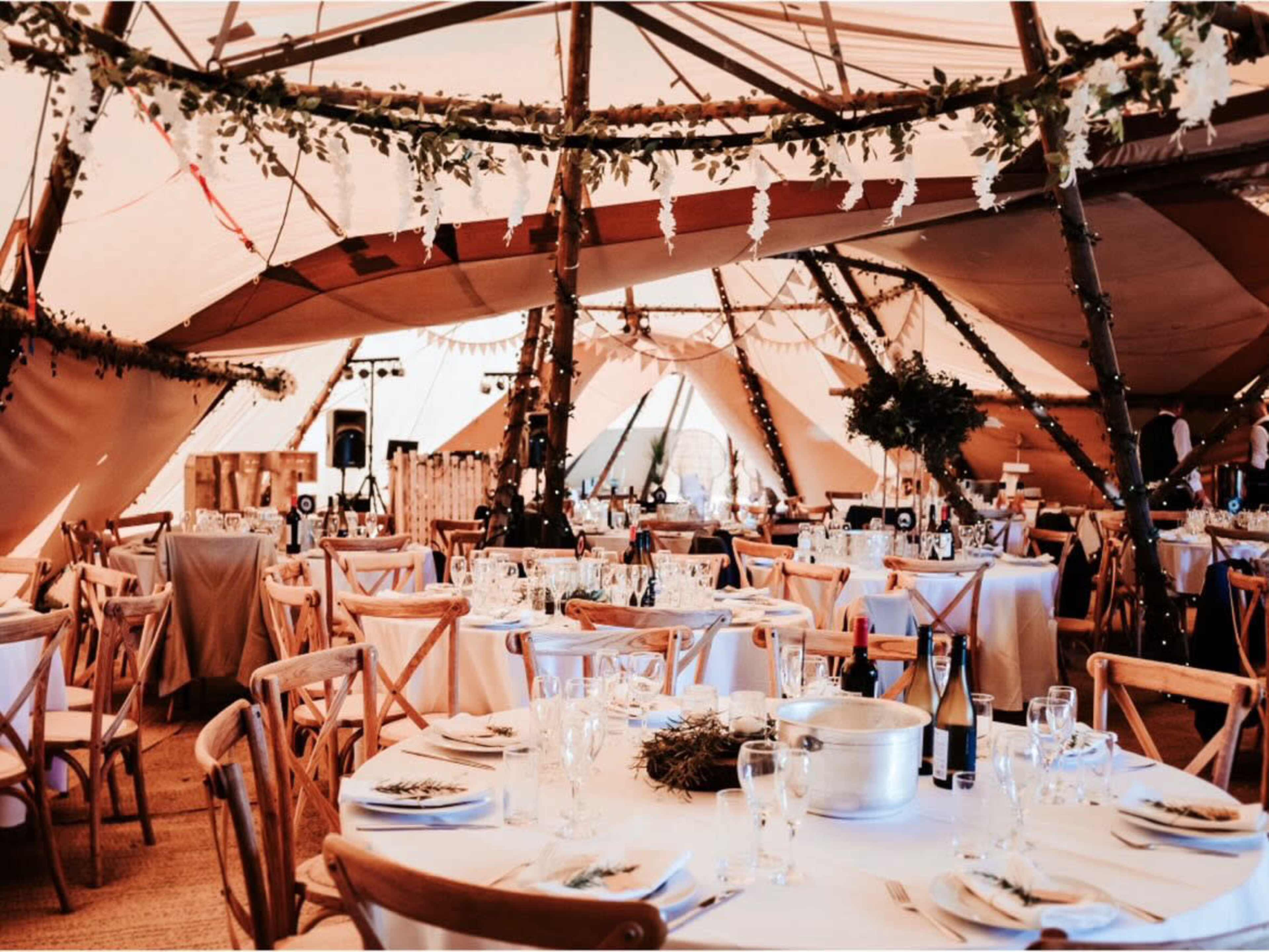 A beautifully set dining area inside a large tent, with tables arranged and decorated with floral arrangements and tableware.